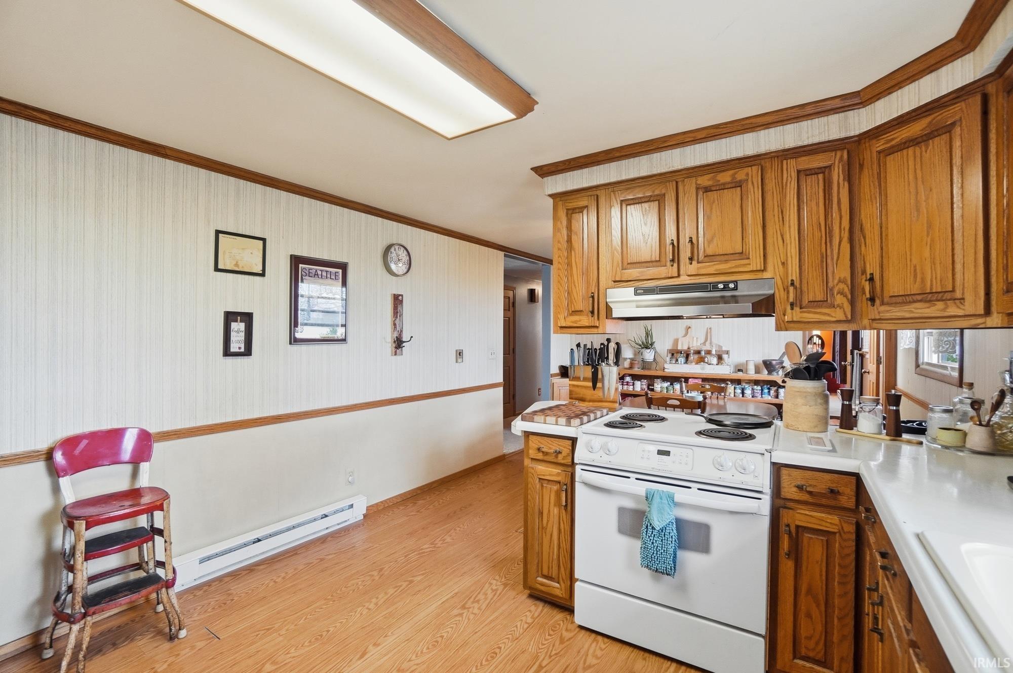 Kitchen featuring crown molding, white electric range oven, light countertops, wood finish cabinets, and light wood-type flooring