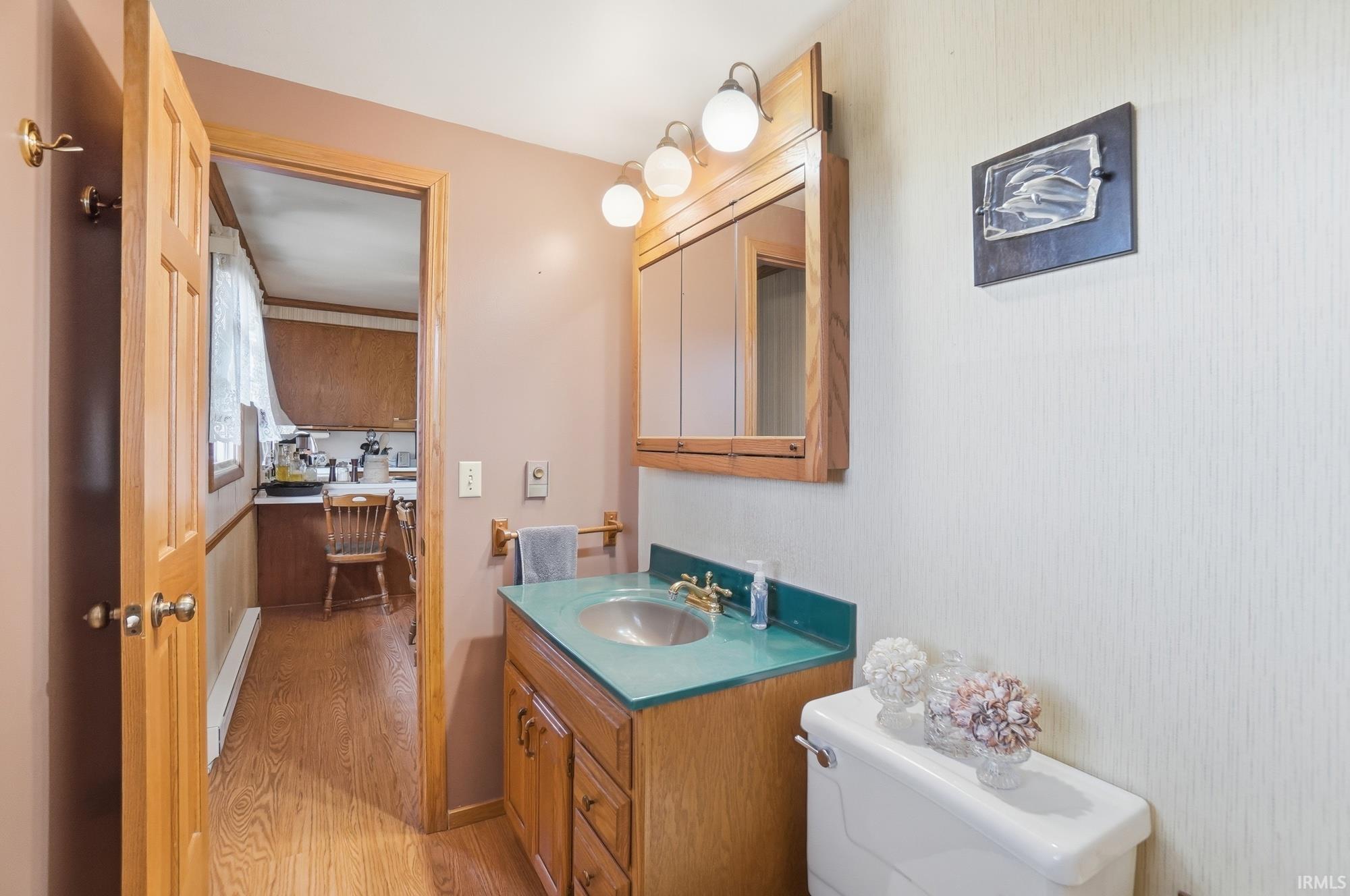 Half bath featuring vanity, light wood-style flooring, and a baseboard heating unit