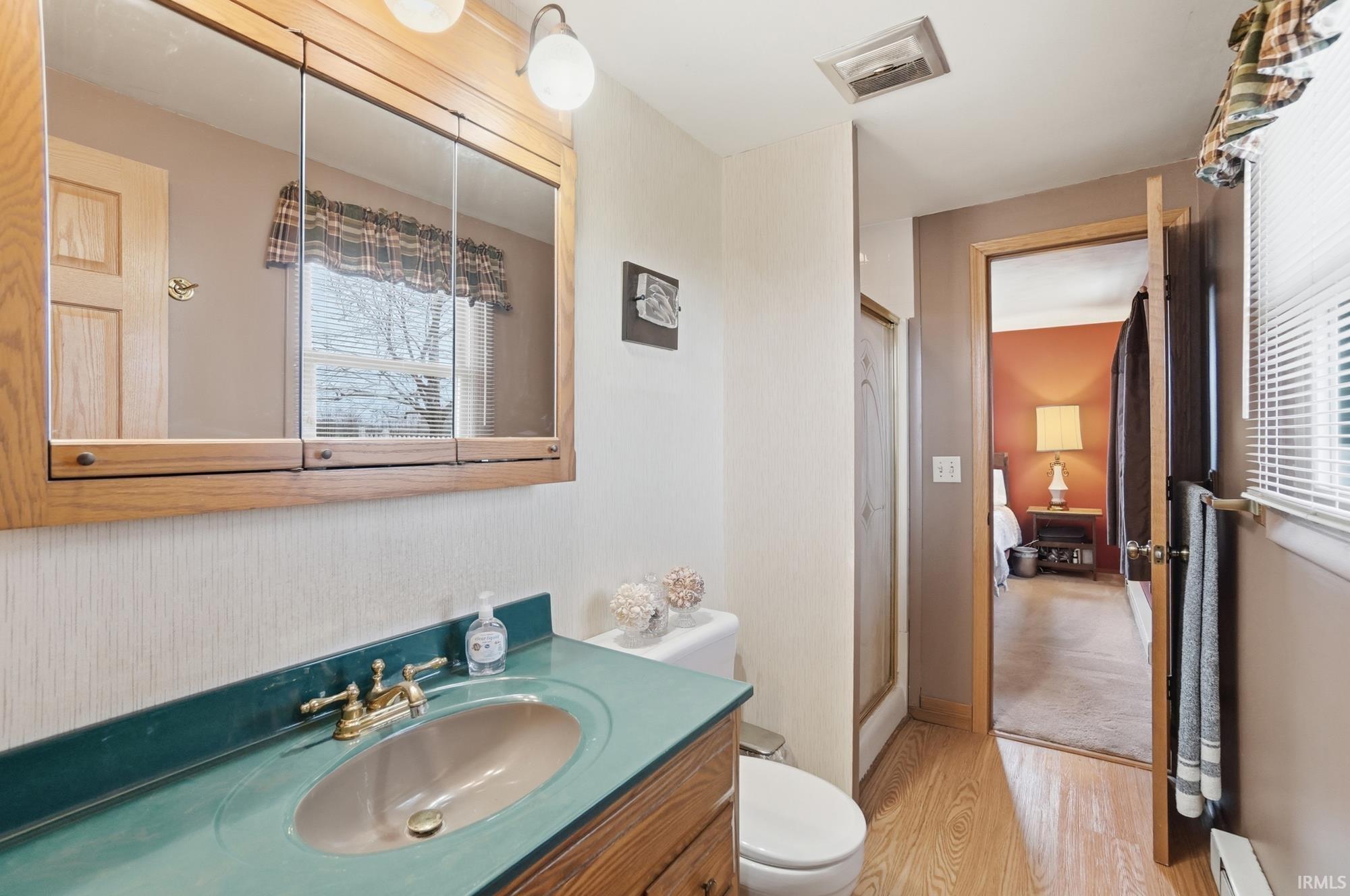 Bathroom with vanity, a shower stall, light wood-style flooring, and baseboard heating