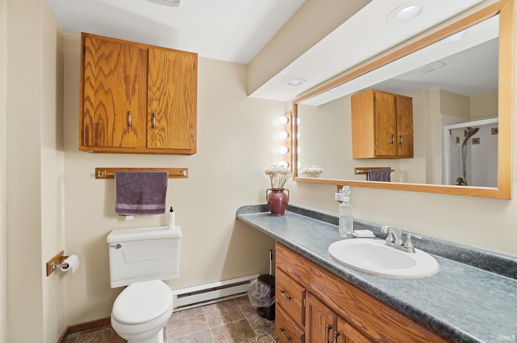 Full bath with a baseboard heating unit, vanity, and a shower stall