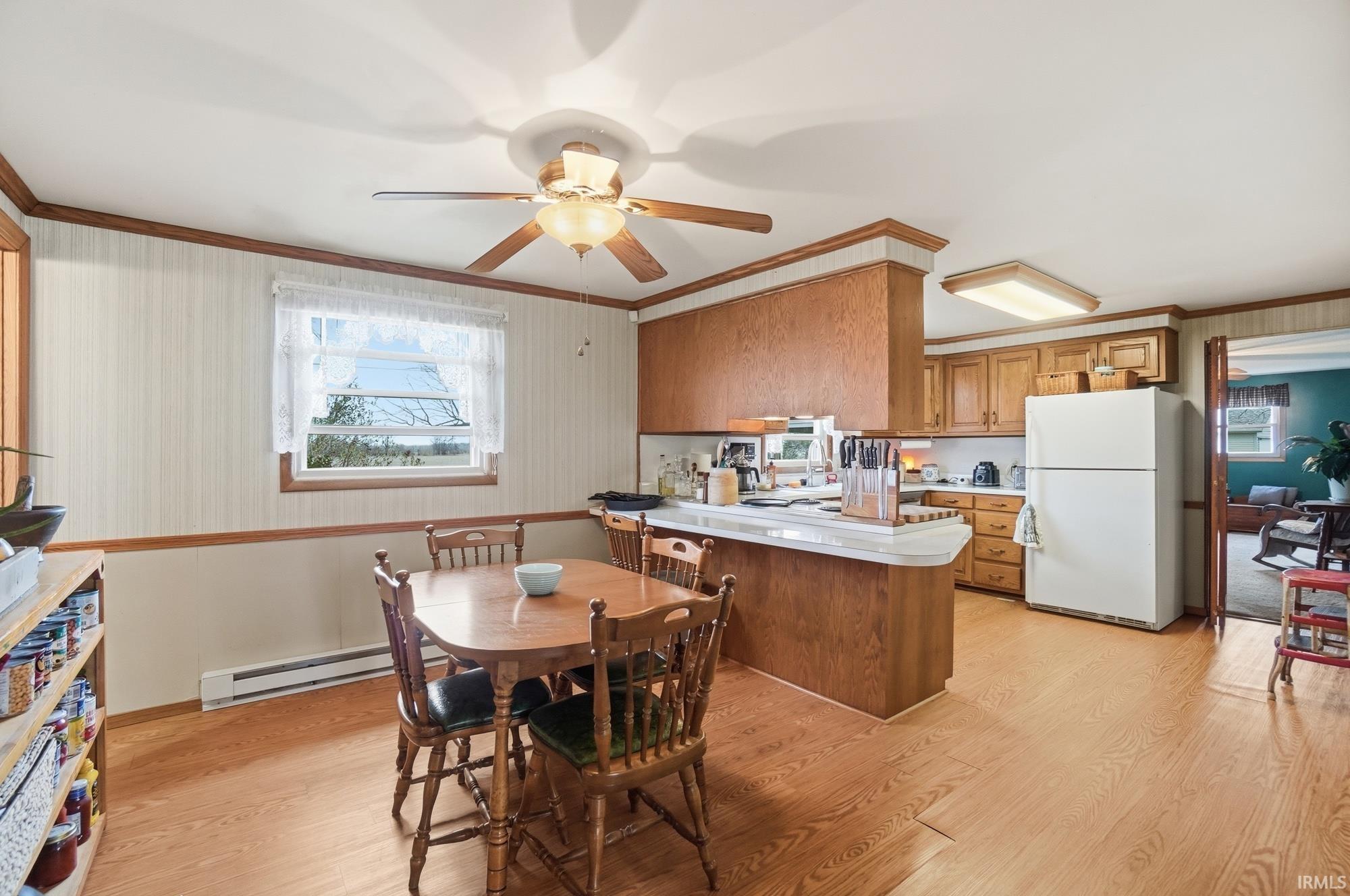 Kitchen featuring wallpapered walls, wood finish cabinetry, a peninsula, light countertops, and freestanding refrigerator
