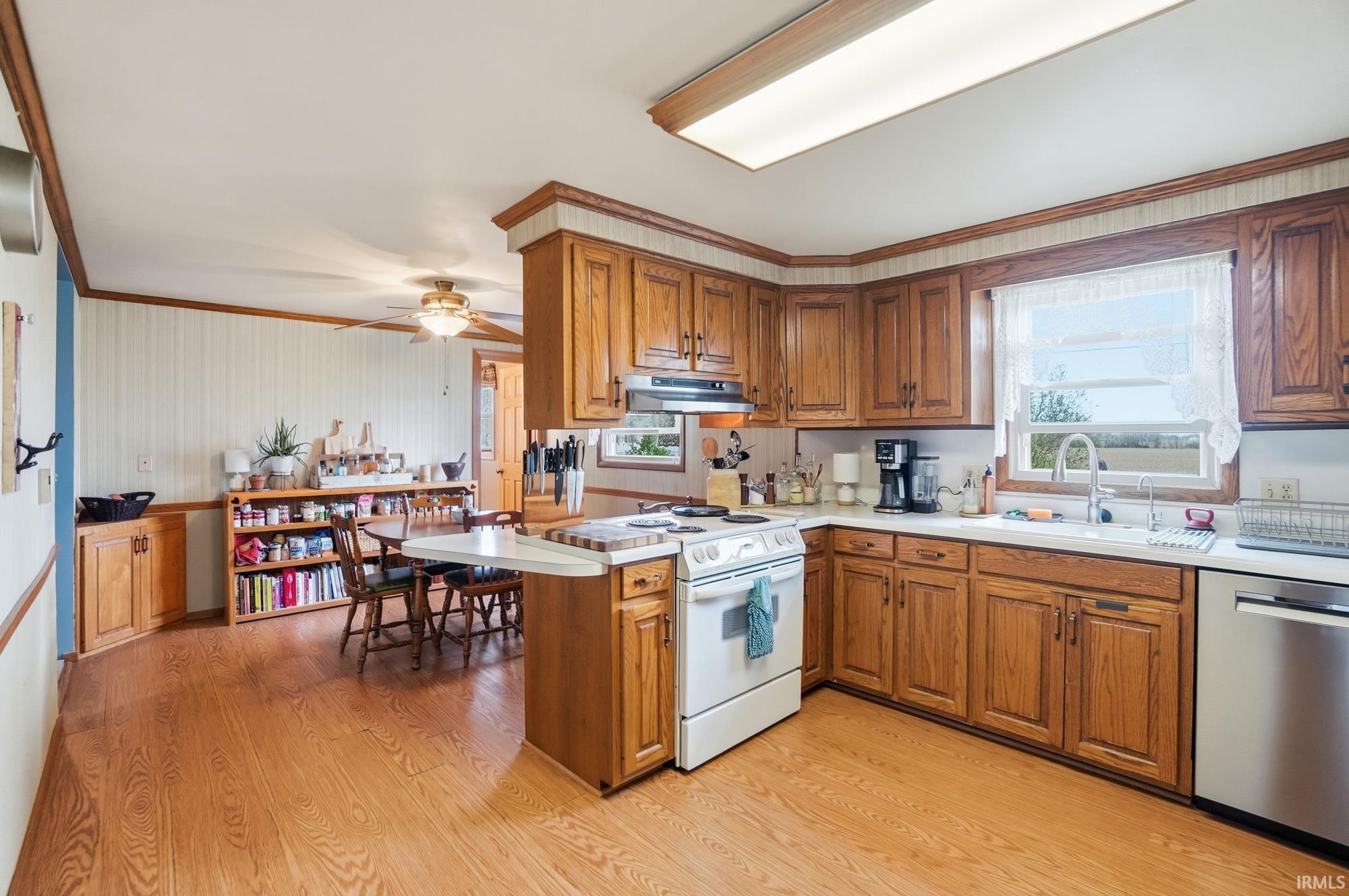 Kitchen with wood finish cabinetry, light countertops, dishwasher, crown molding, and a peninsula
