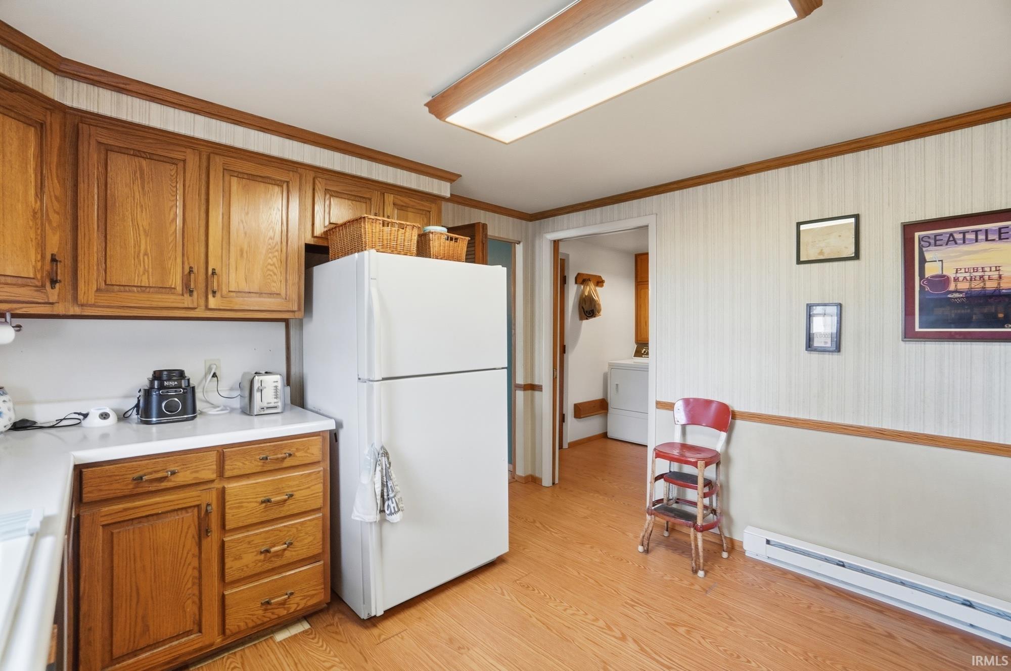 Kitchen featuring wood finish cabinets, freestanding refrigerator, baseboard heating, light countertops, and crown molding
