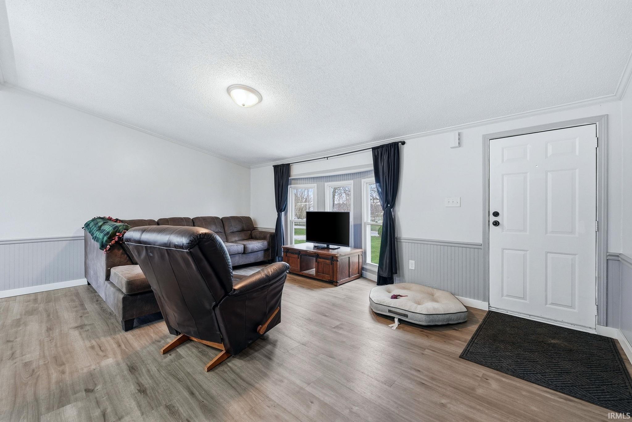 Living area with a wainscoted wall, a textured ceiling, and light wood-type flooring