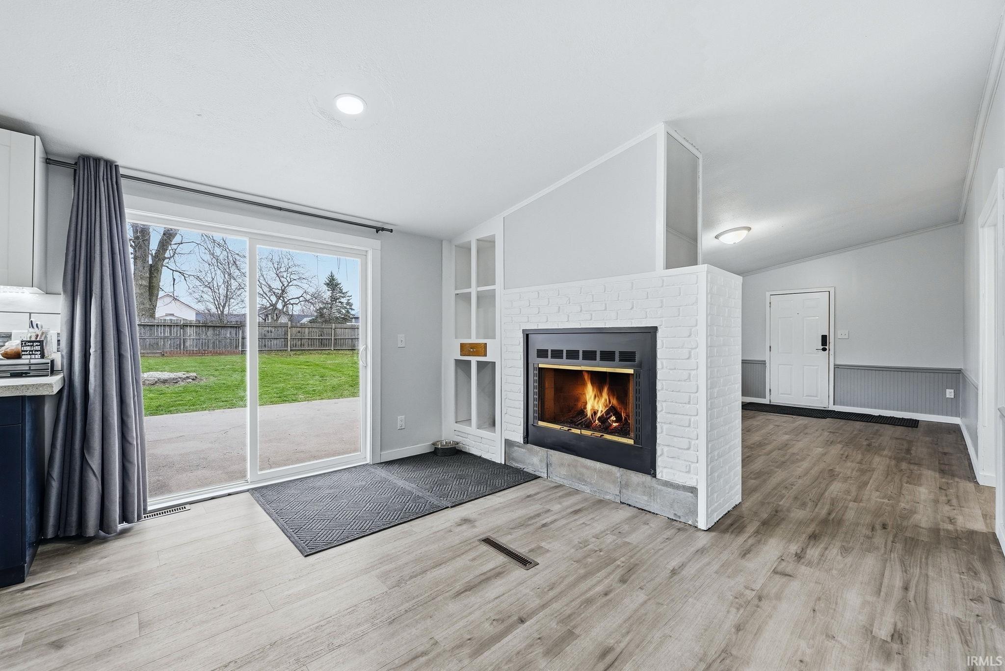 Unfurnished living room with a fireplace, lofted ceiling, wainscoting, and light wood finished floors