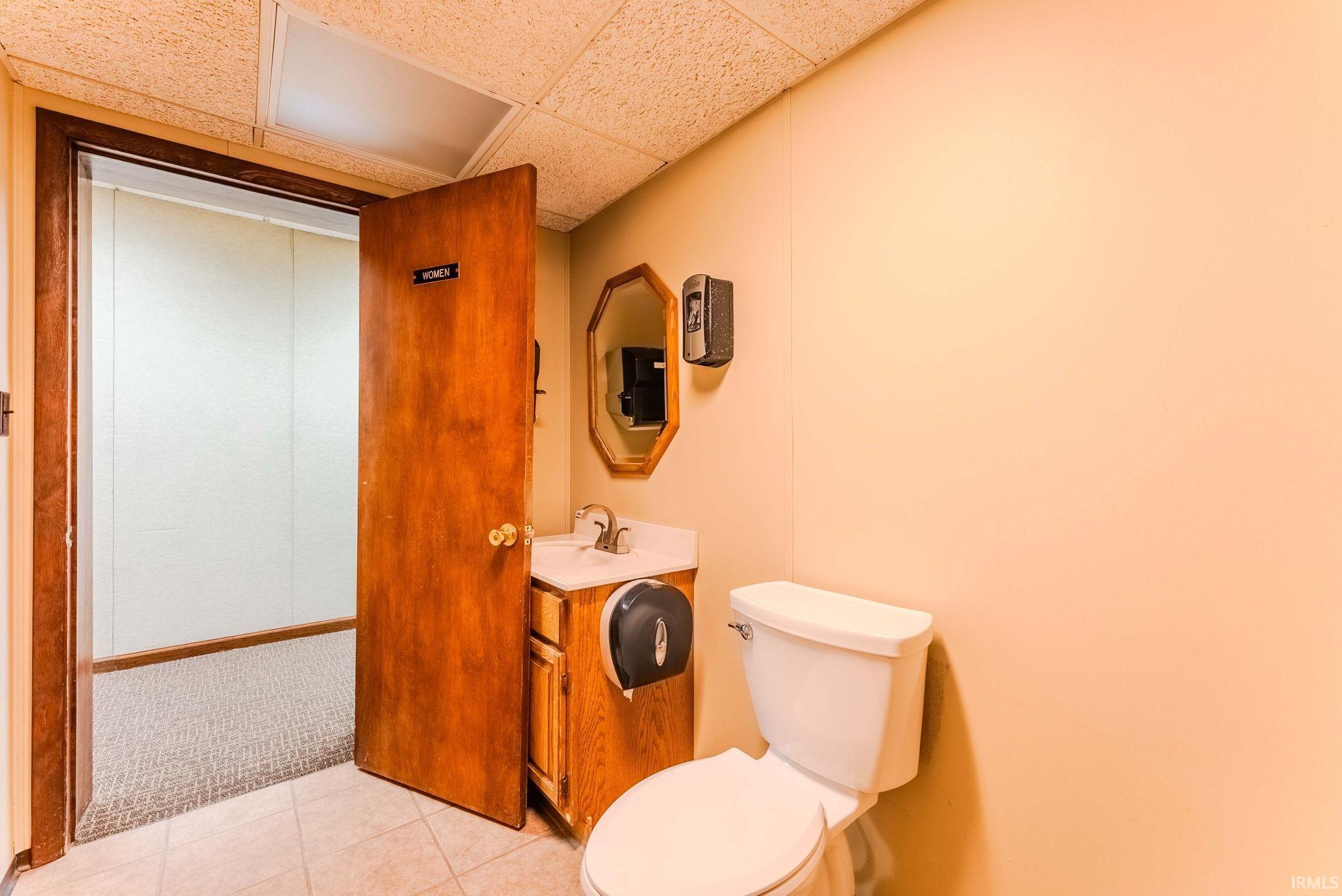 Half bathroom with vanity, a paneled ceiling, light colored carpet, and light tile patterned floors