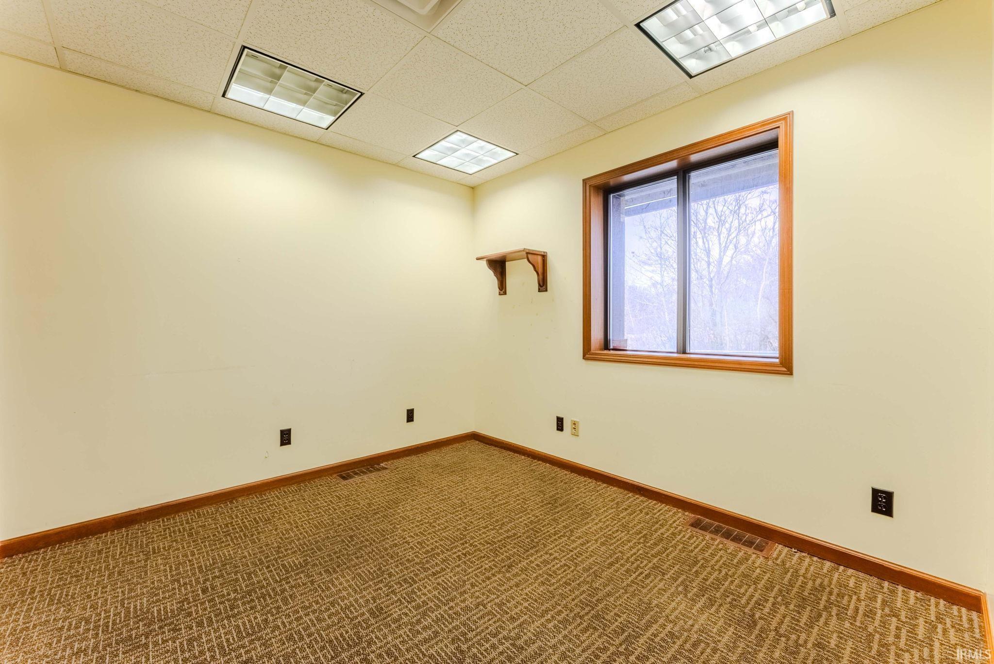Carpeted empty room with a drop ceiling and baseboards