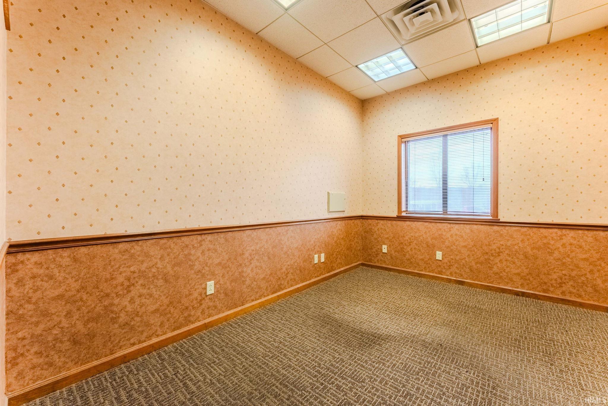 Empty room featuring a paneled ceiling, carpet flooring, and wallpapered walls