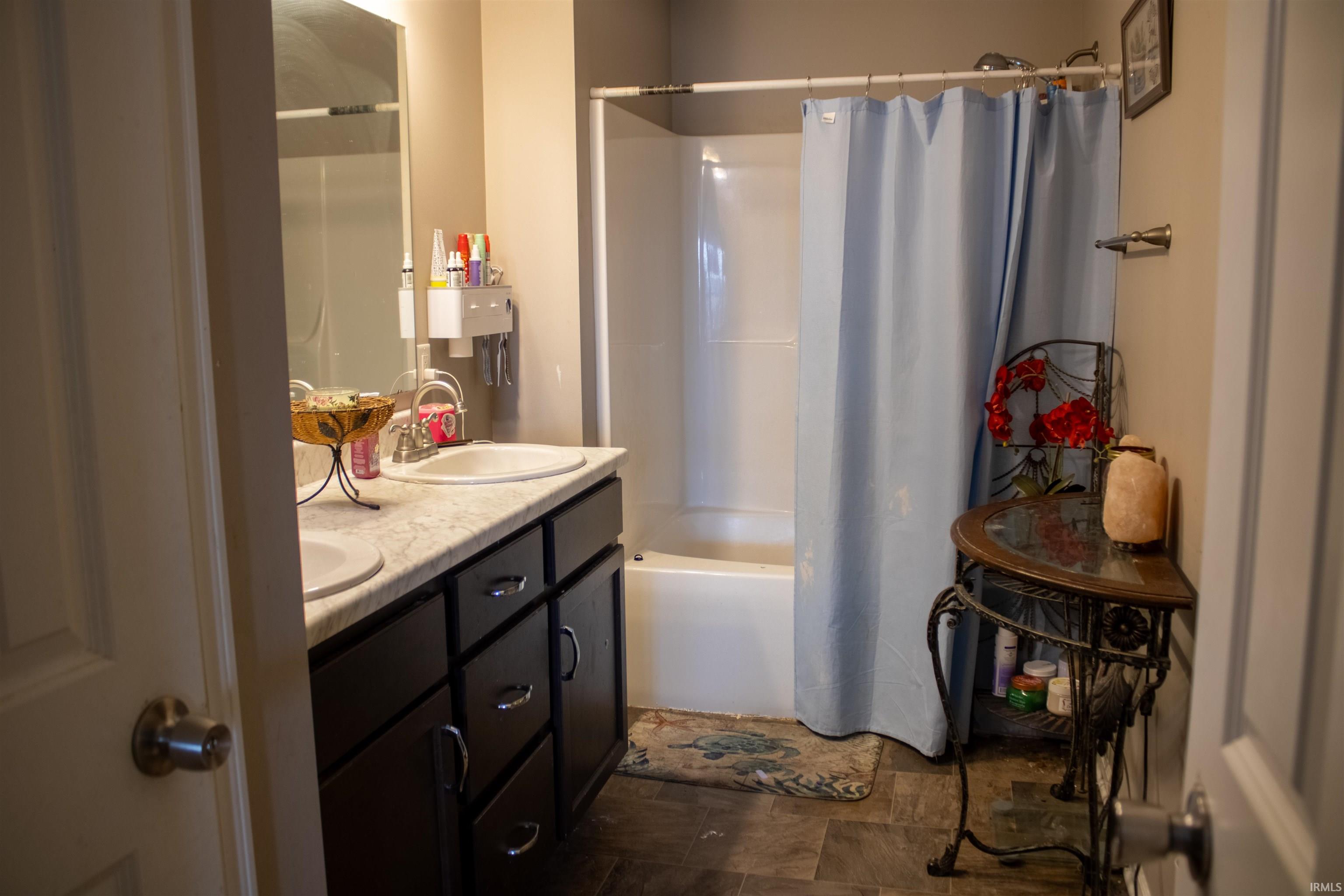 Bathroom featuring double vanity, shower / bath combo with shower curtain, and stone finish flooring