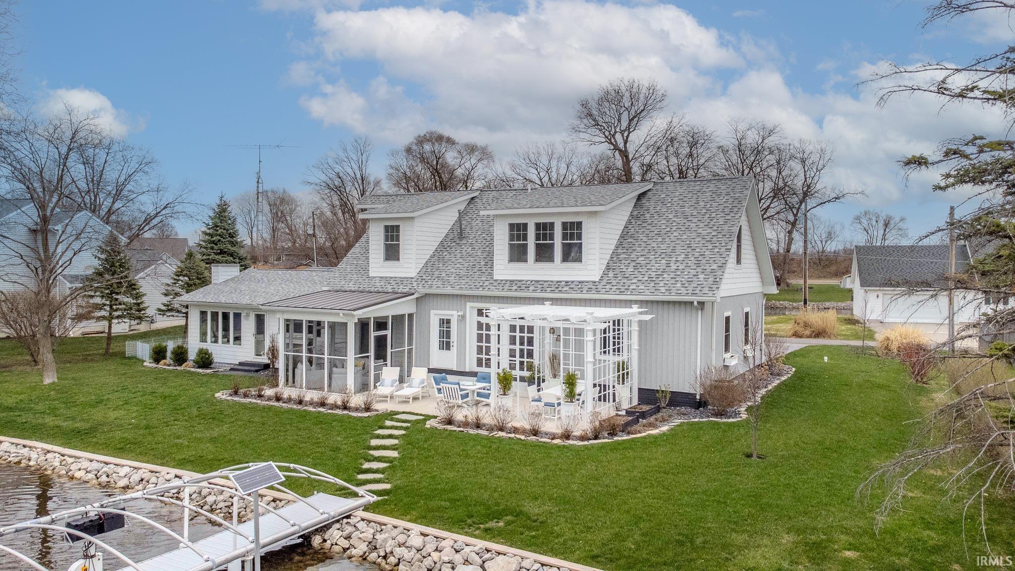 Back of property featuring a sunroom, roof with shingles, a lawn, a patio area, and a water view