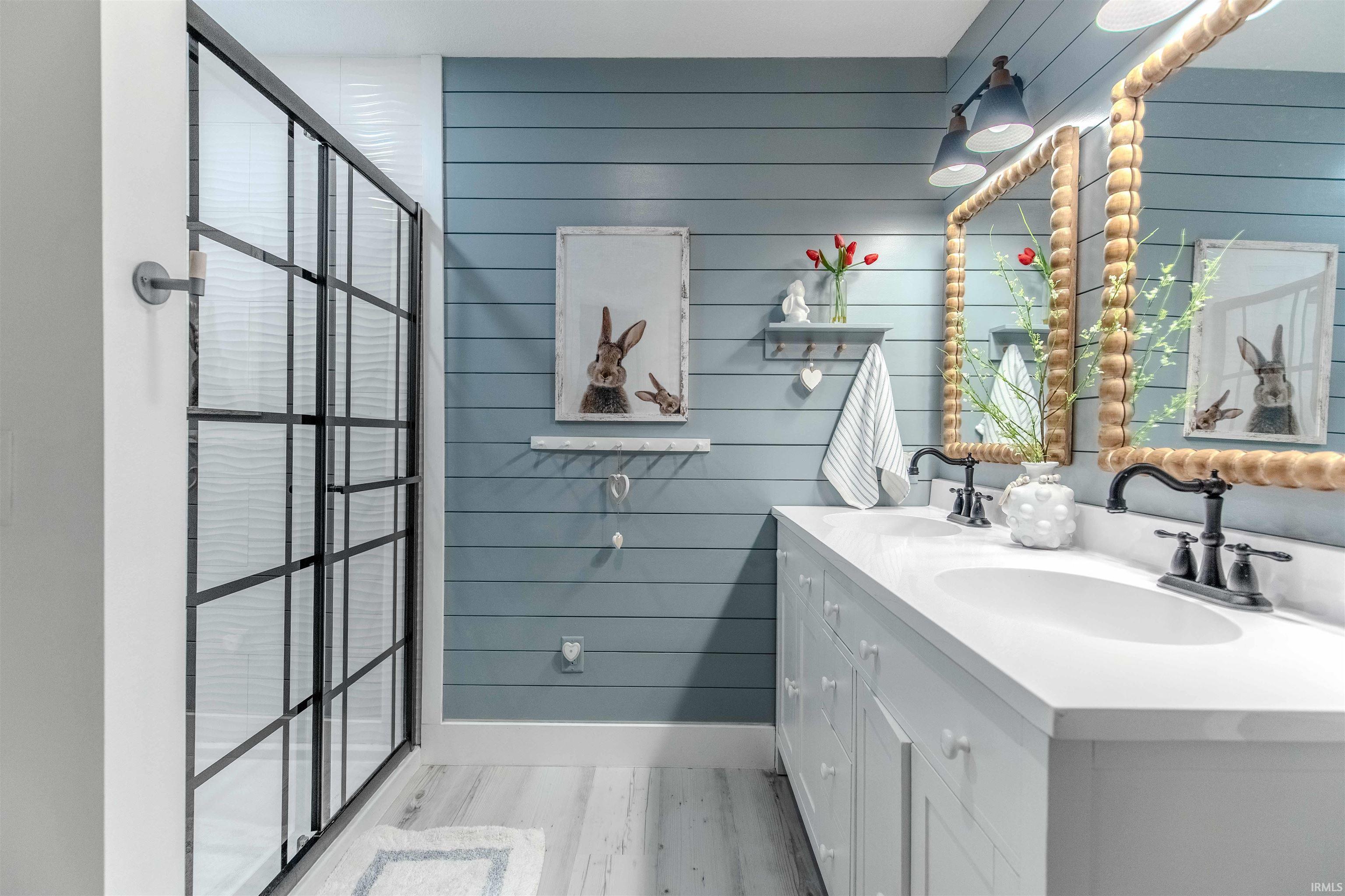 Bathroom with wood walls, double vanity, light wood-style floors, and a walk in shower