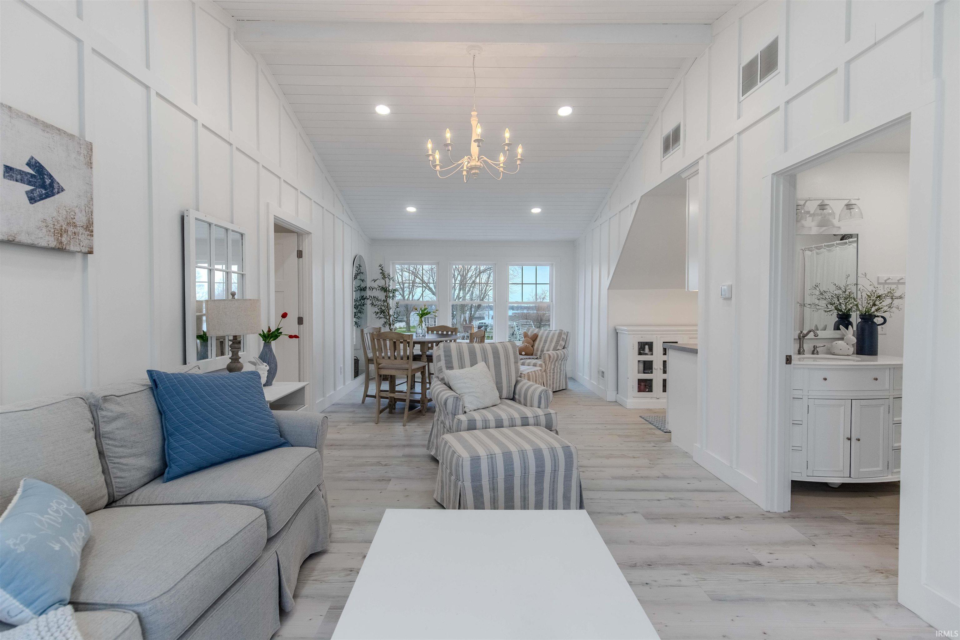 Living area featuring a decorative wall, vaulted ceiling, light wood-style floors, and suspended lighting