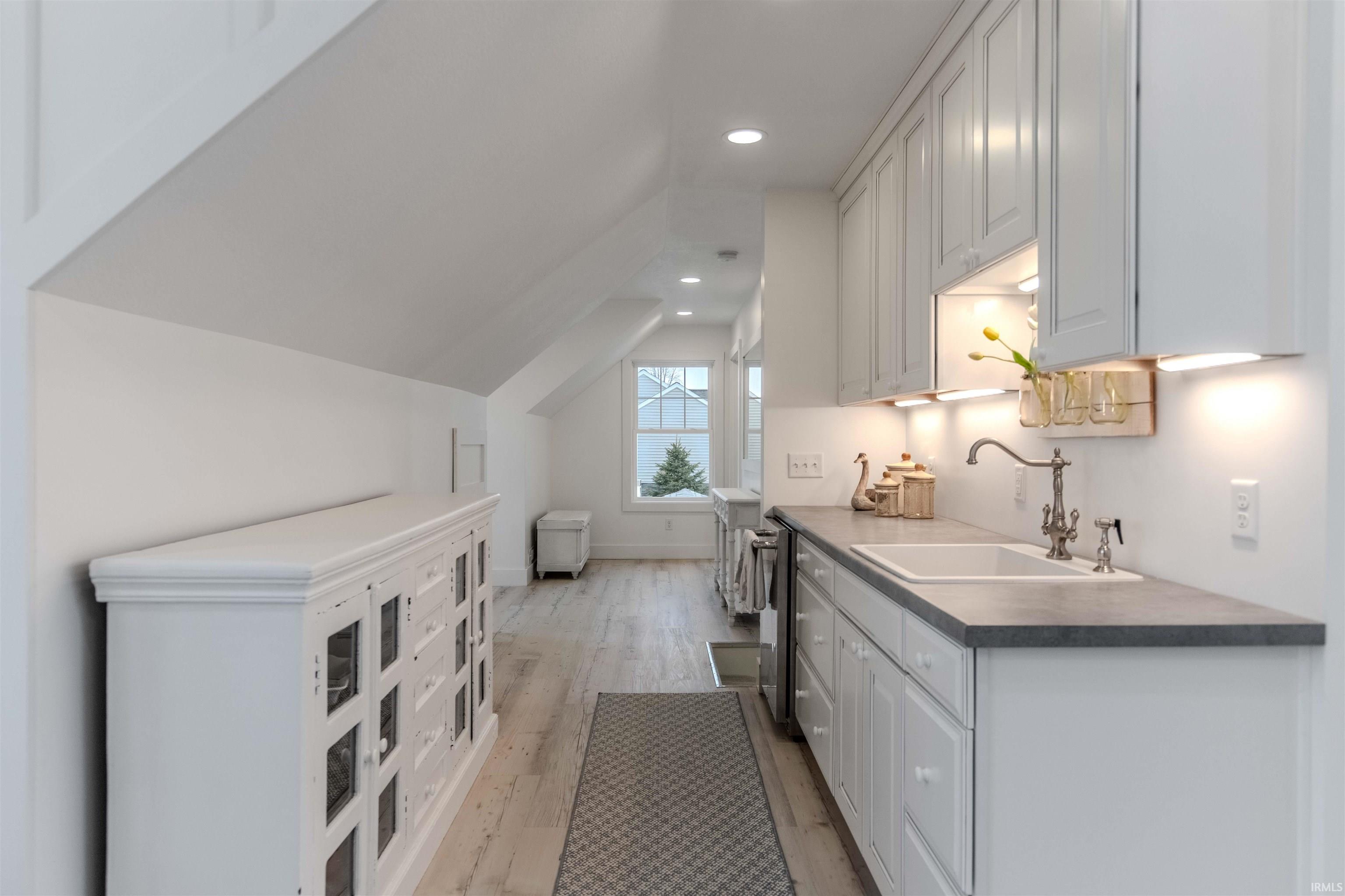 Kitchen featuring lofted ceiling, light wood-style flooring, white cabinetry, dark countertops, and stainless steel dishwasher