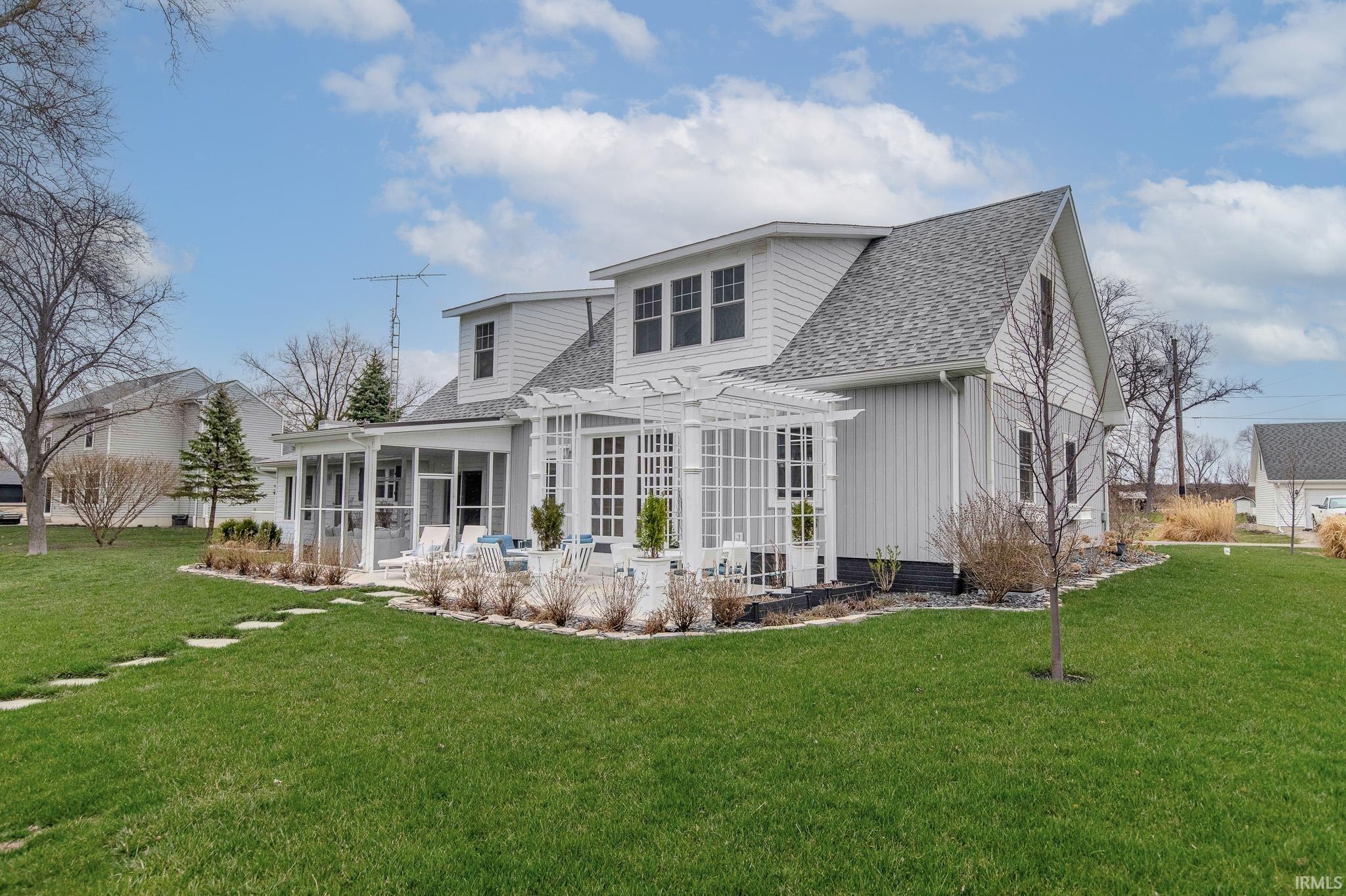 Rear view of property featuring a sunroom, roof with shingles, a yard, and a pergola
