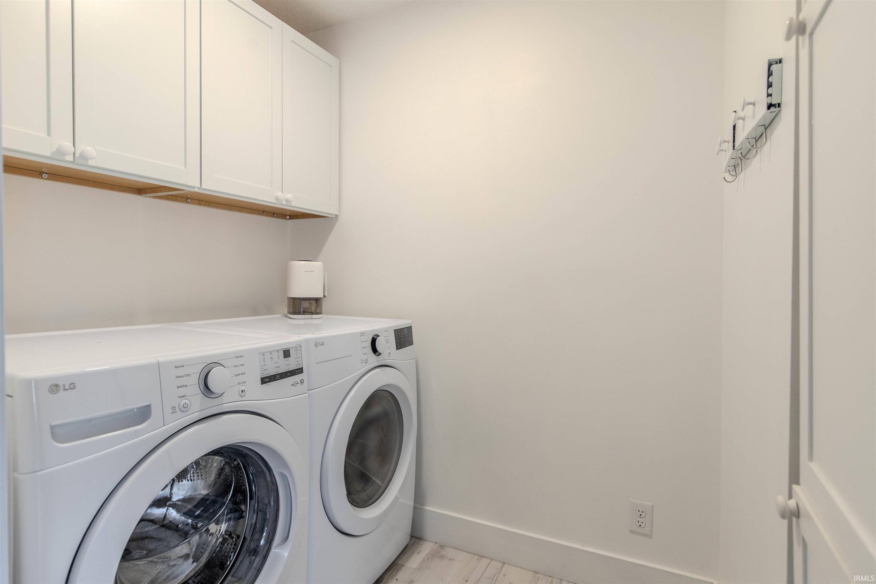Laundry area featuring washer and dryer, cabinet space, and light wood-style flooring
