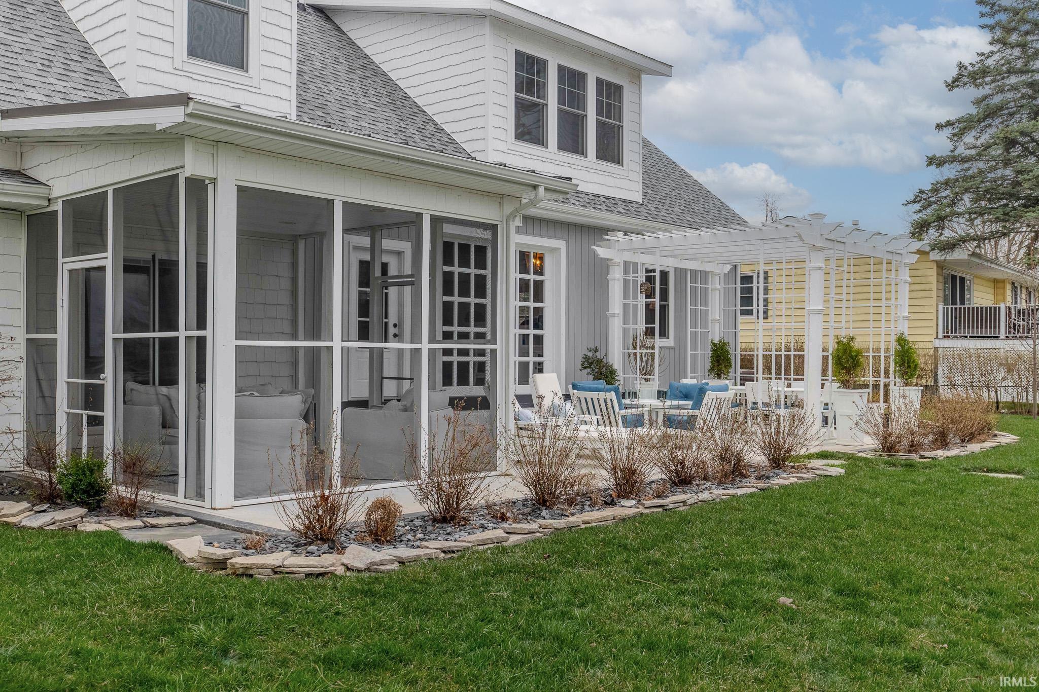 Back of house with a shingled roof, a lawn, a patio area, and a sunroom