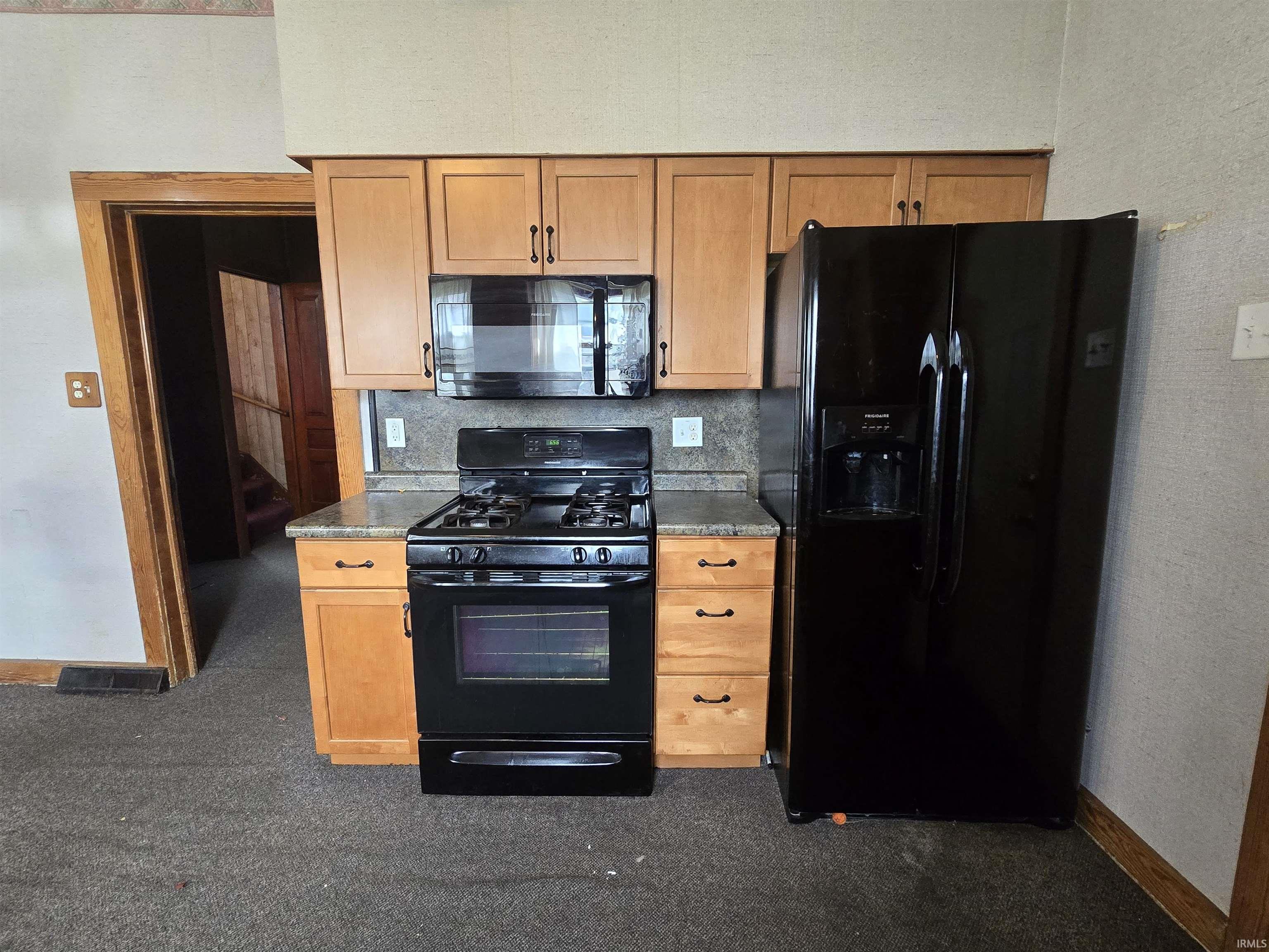 Kitchen featuring black appliances, a textured wall, tasteful backsplash, dark countertops, and light wood finish cabinetry