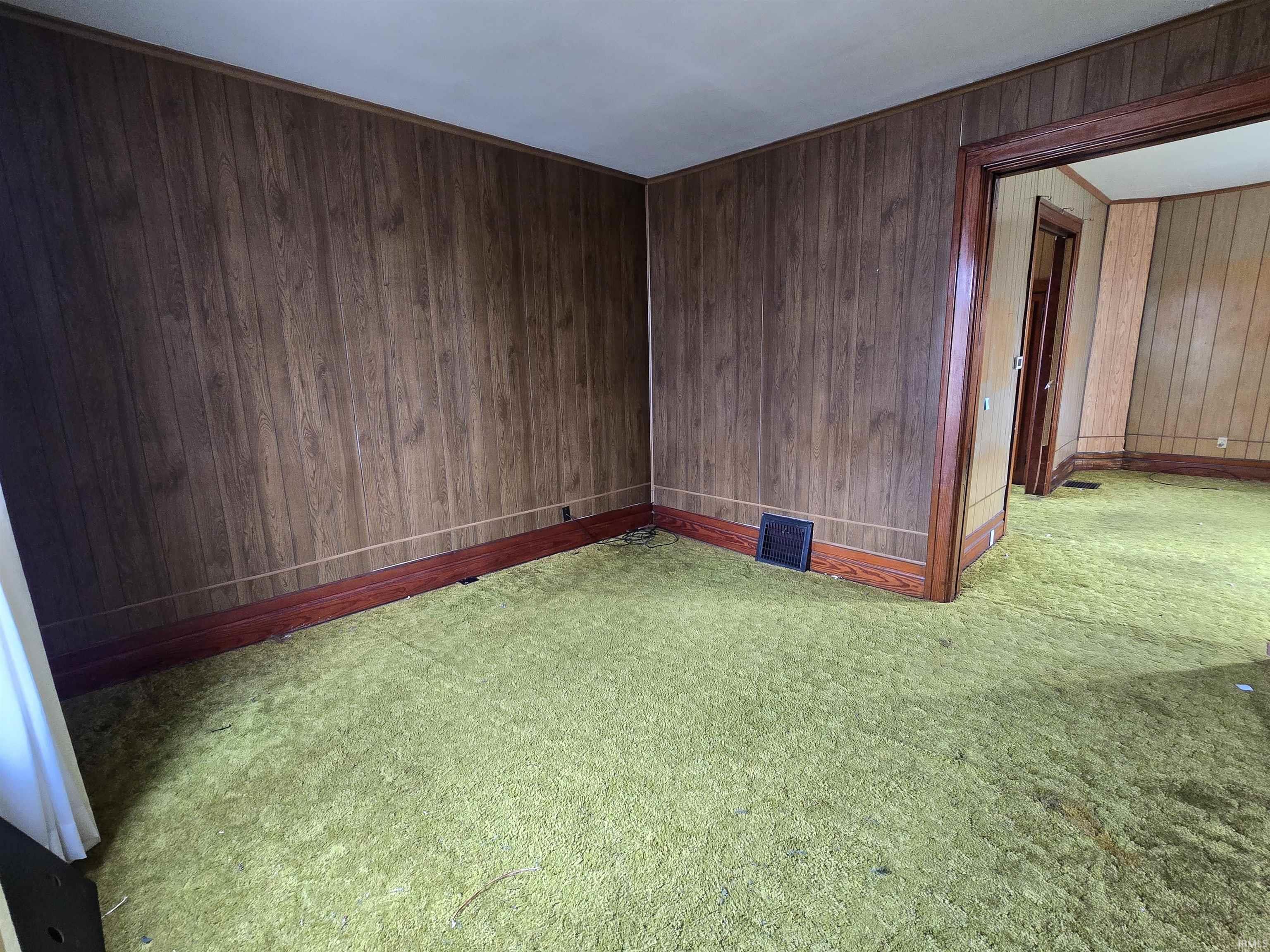 Carpeted empty room featuring wooden walls and baseboards