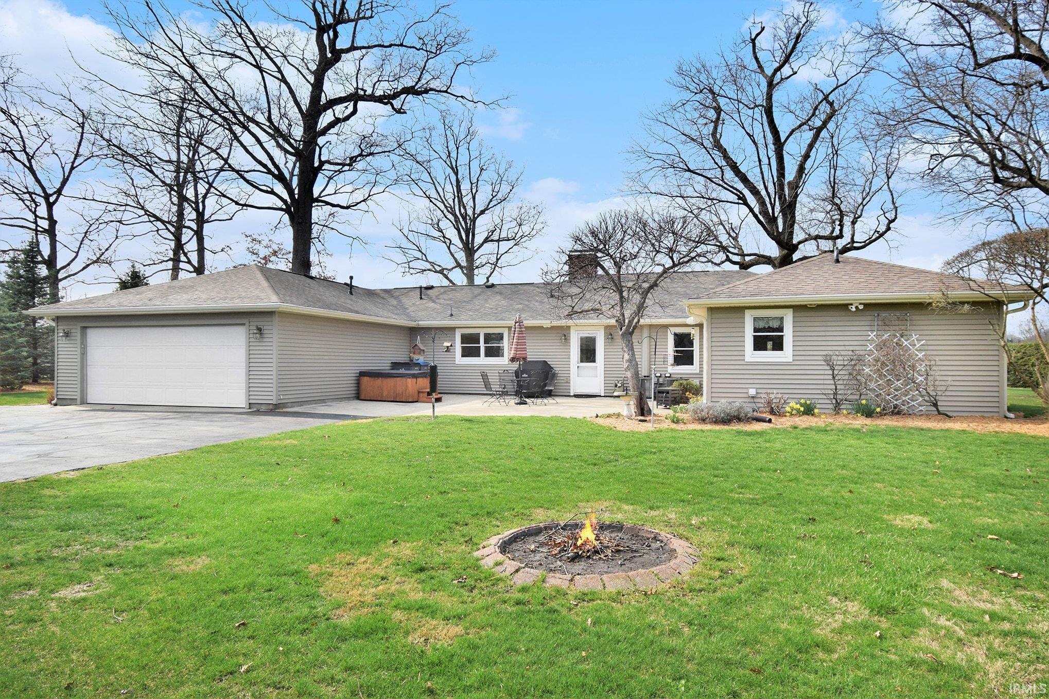 Rear view of house with an attached garage, a patio area, driveway, and a yard