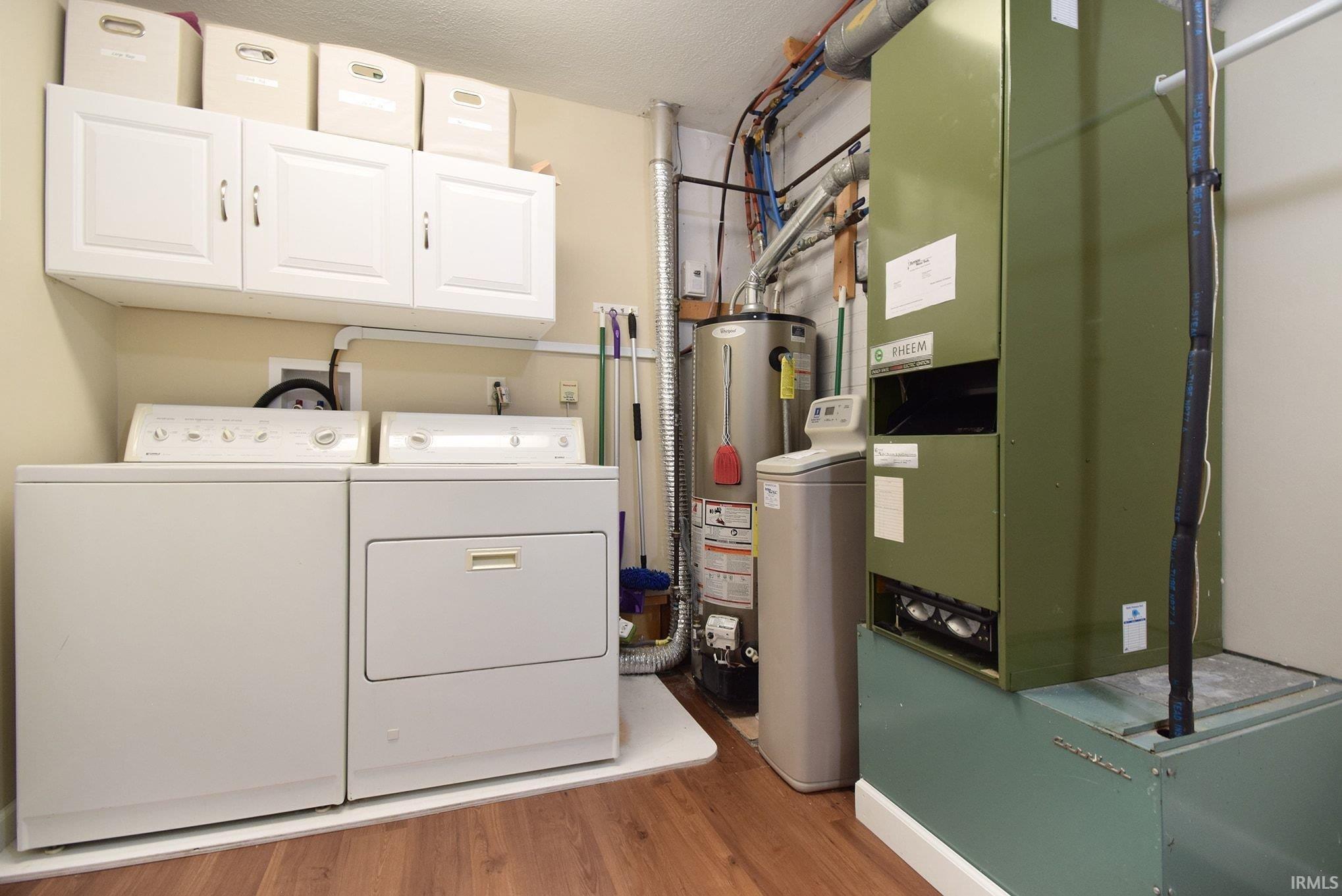 Laundry room with cabinet space, water heater, washing machine and clothes dryer, light wood-type flooring, and heating unit