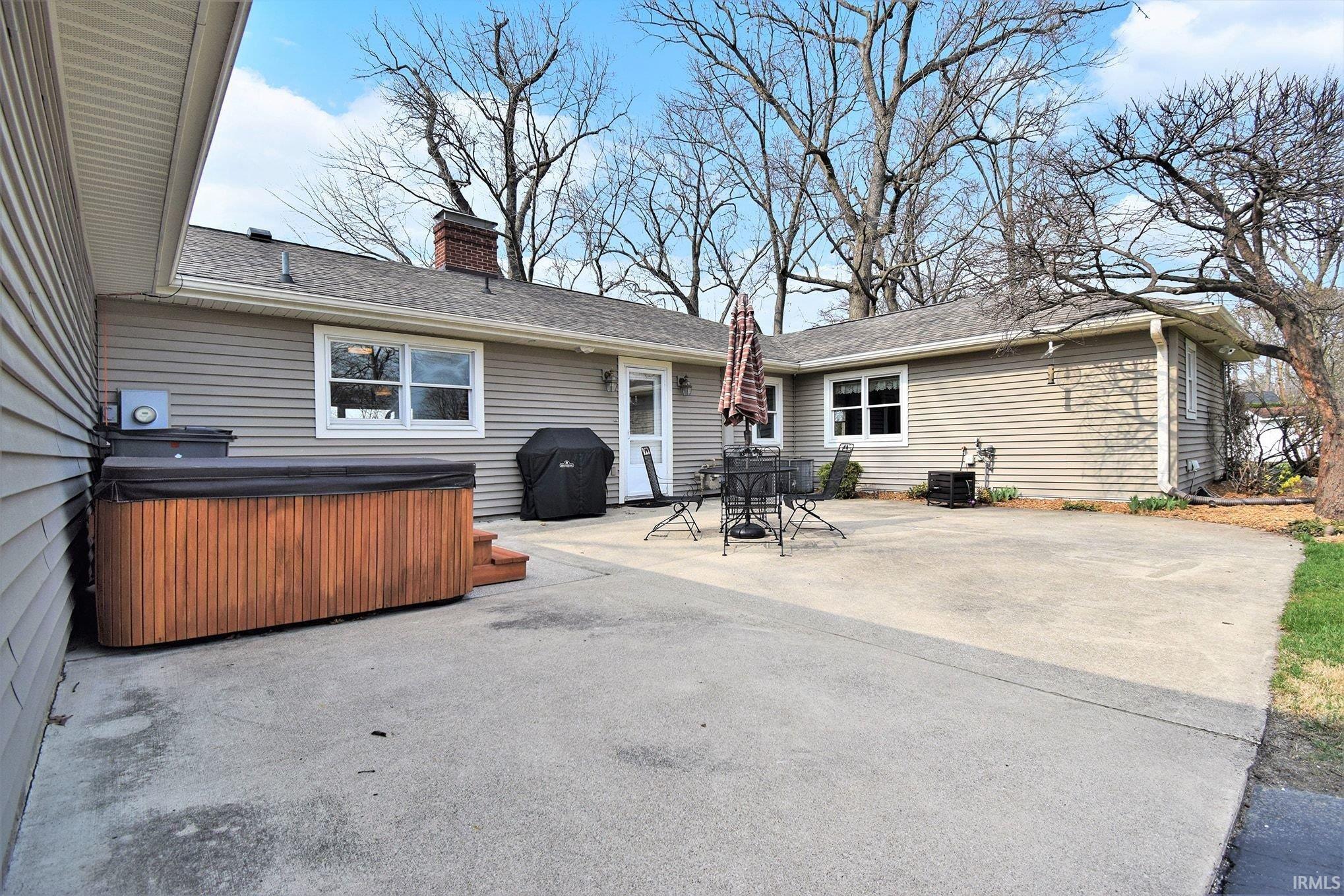 Back of property featuring a hot tub, a patio, a chimney, roof with shingles, and outdoor dining area