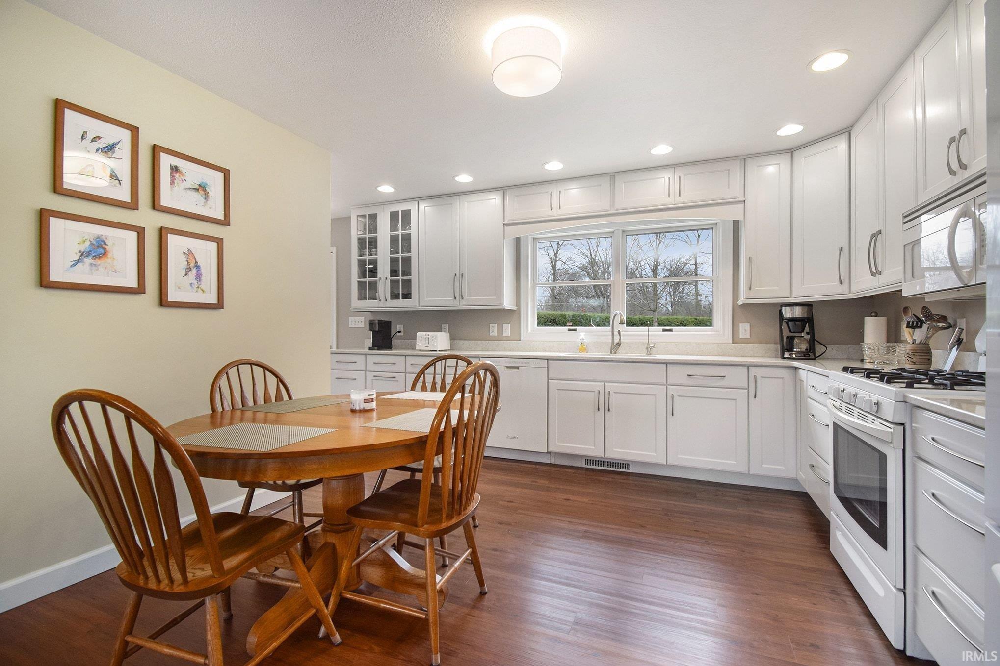 Kitchen featuring white appliances, white cabinetry, recessed lighting, dark wood-type flooring, and light stone counters