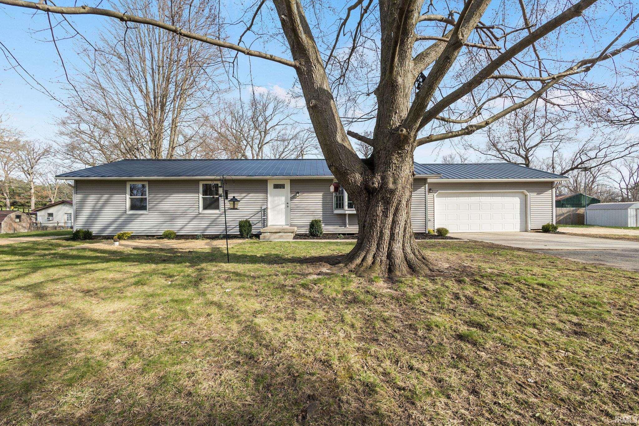 Ranch-style house with driveway, a metal roof, an attached garage, and a front lawn