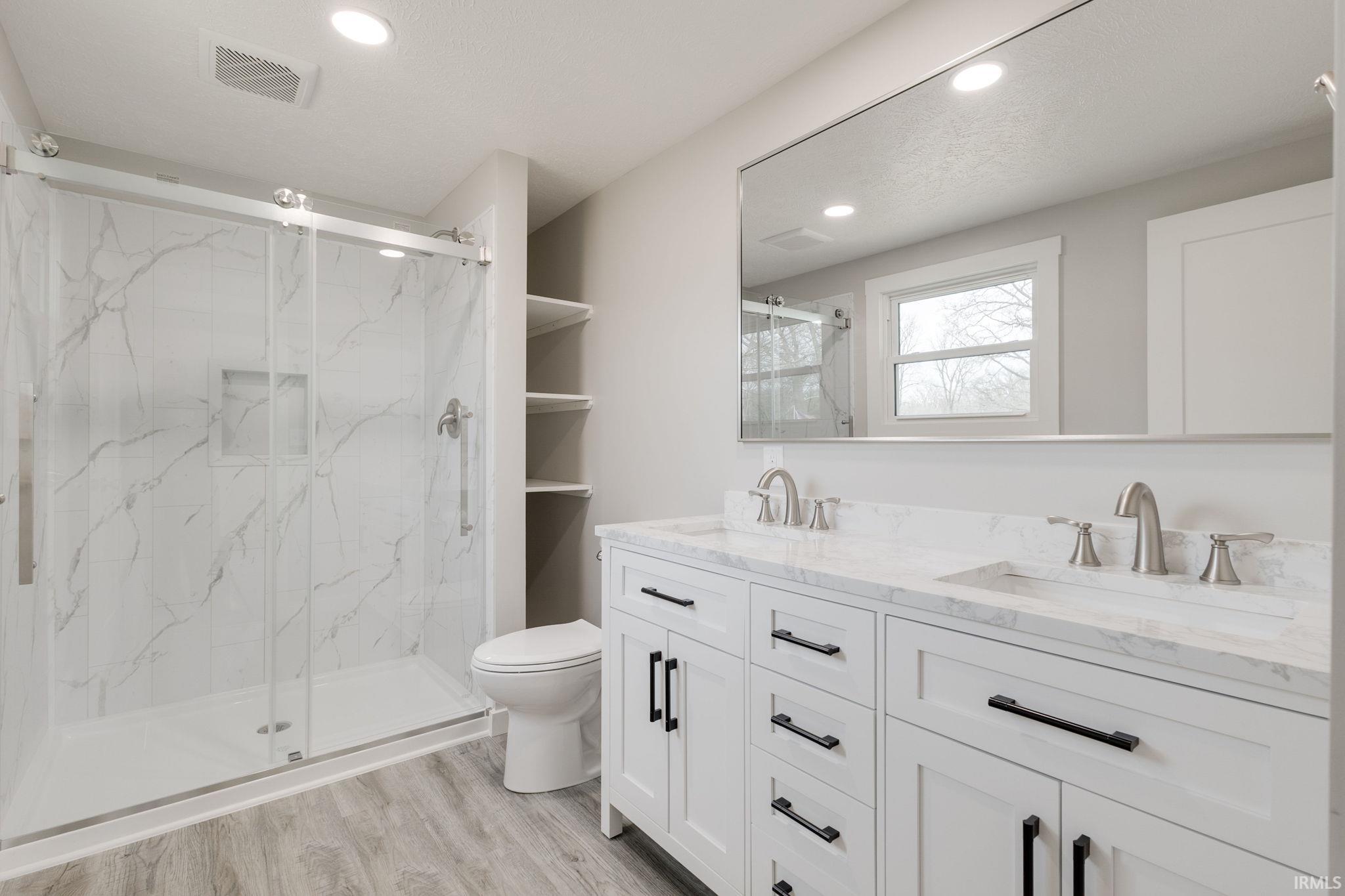 Bathroom featuring double vanity, a marble finish shower, light wood-type flooring, and recessed lighting