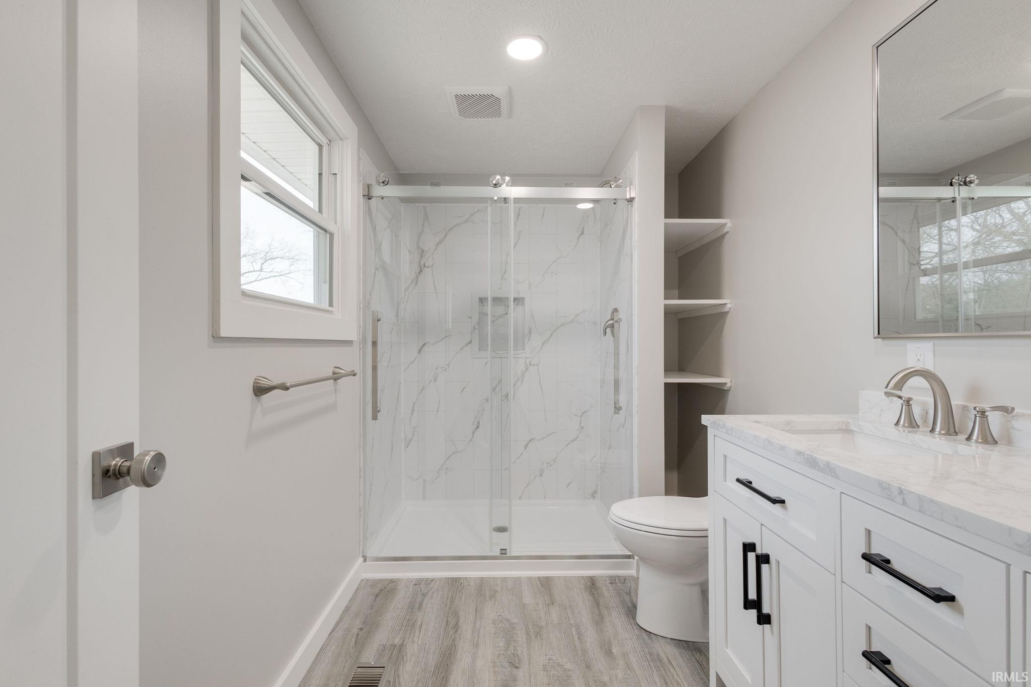 Full bath featuring vanity, a marble finish shower, and light wood-type flooring