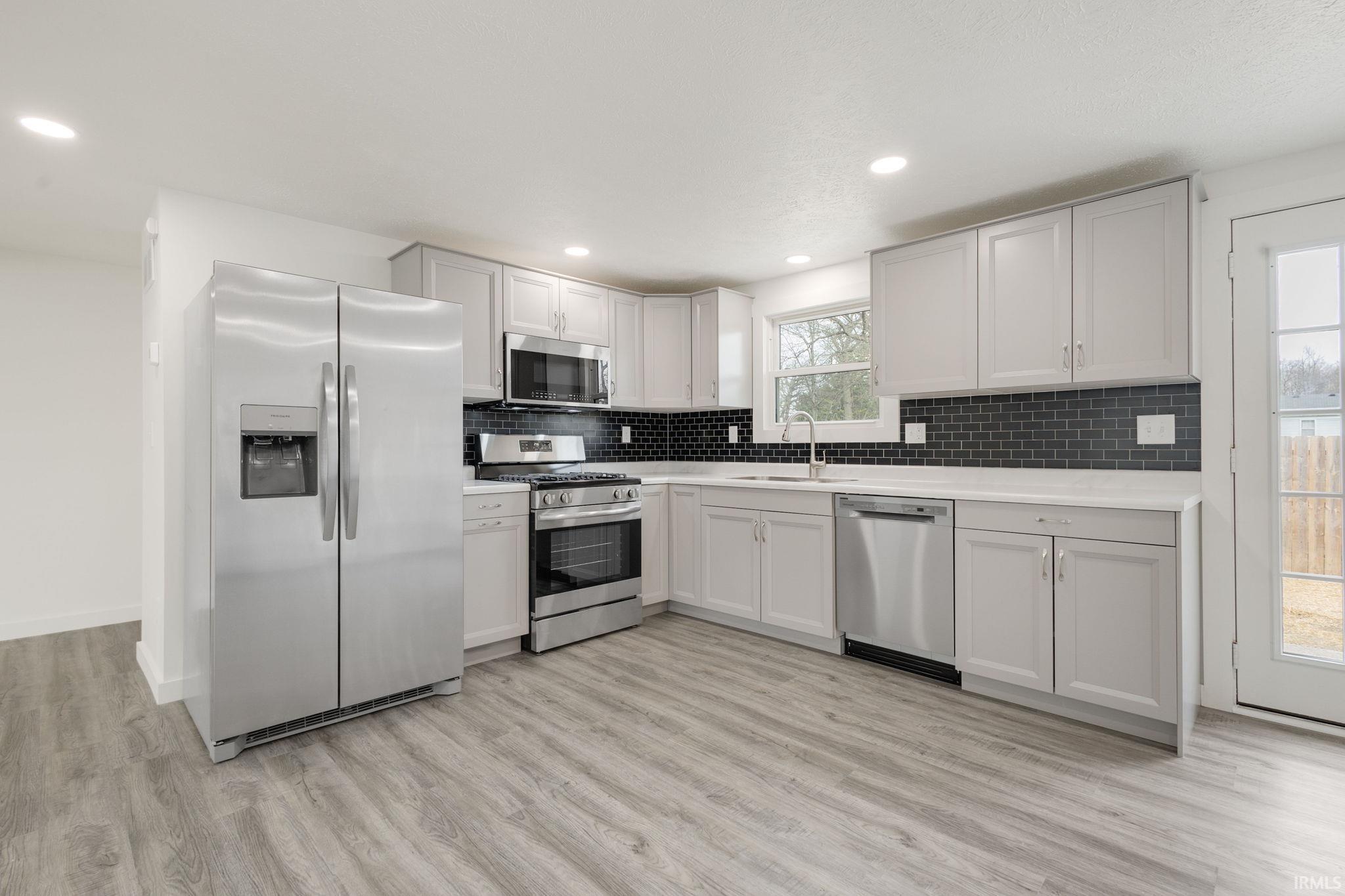 Kitchen featuring stainless steel appliances, decorative backsplash, light wood-type flooring, and recessed lighting