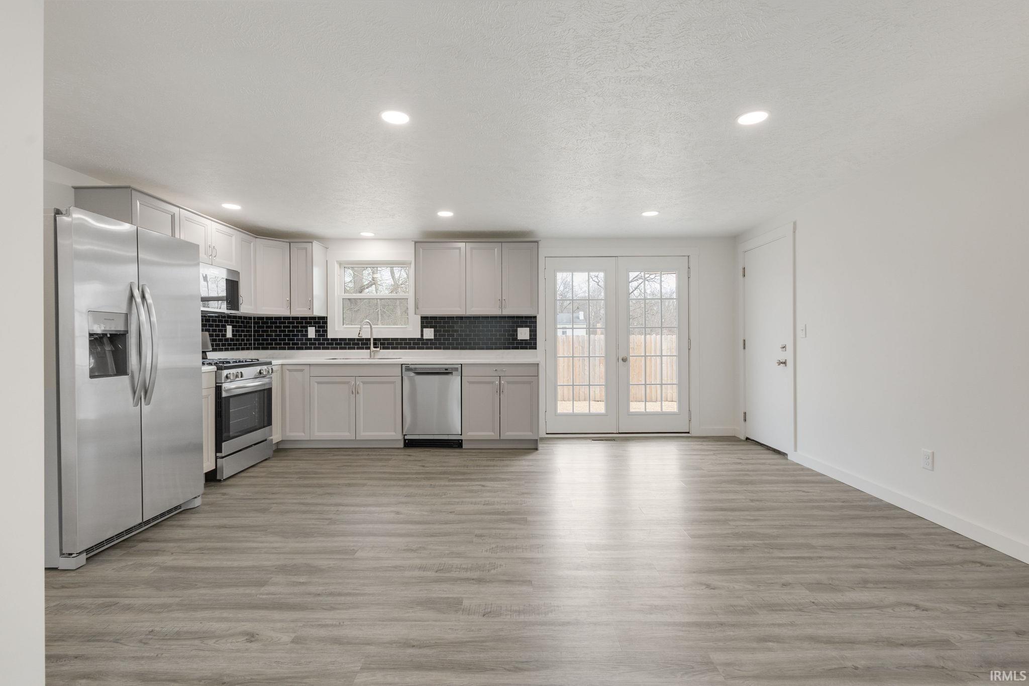 Kitchen with stainless steel appliances, recessed lighting, light countertops, light wood-style flooring, and decorative backsplash