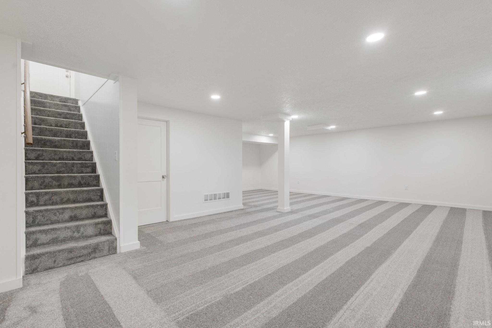 Finished below grade area featuring light colored carpet and recessed lighting