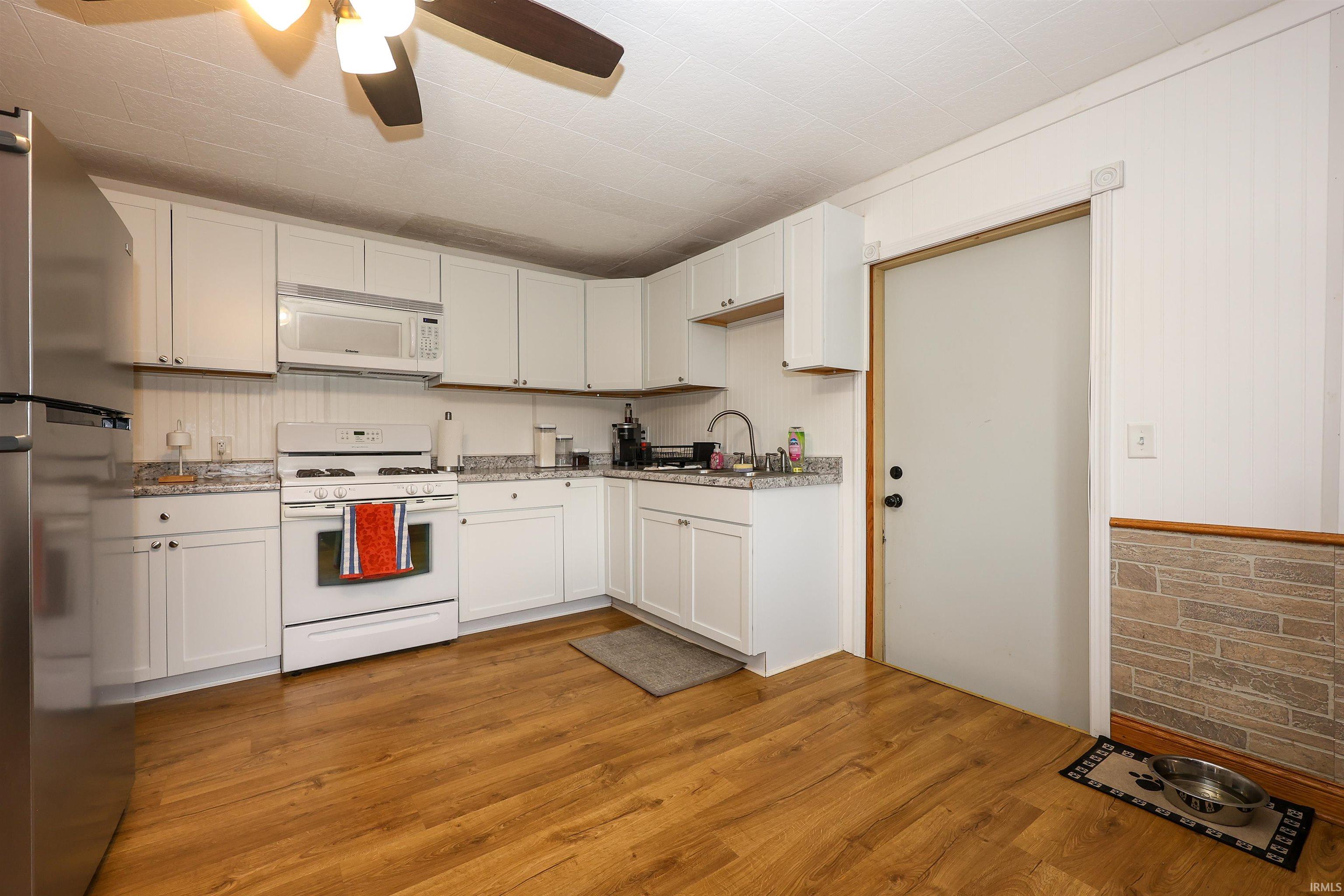 Kitchen featuring white appliances, ceiling fan, white cabinetry, light wood-style flooring, and light stone countertops