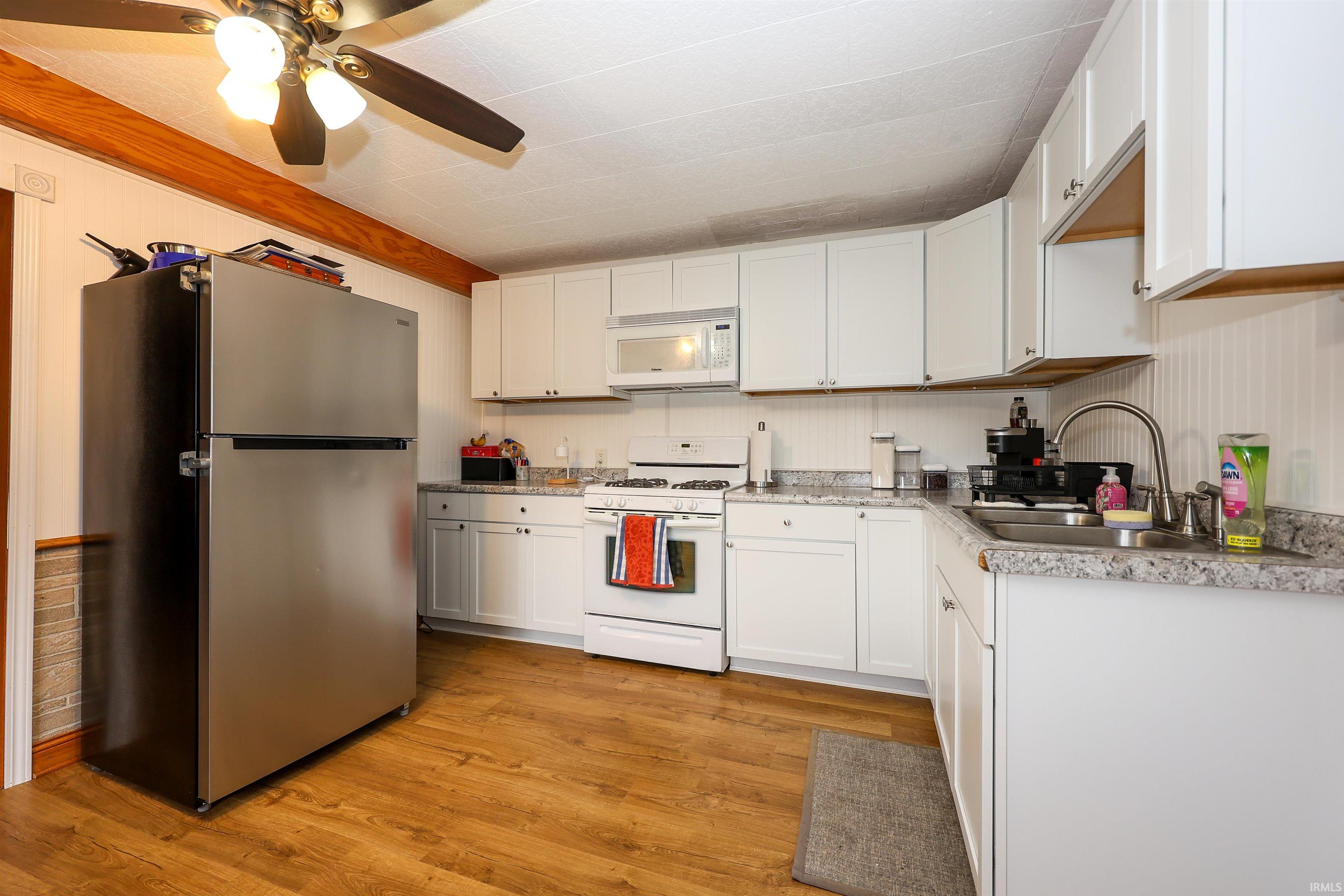 Kitchen with white appliances, light countertops, light wood-type flooring, white cabinetry, and wooden walls