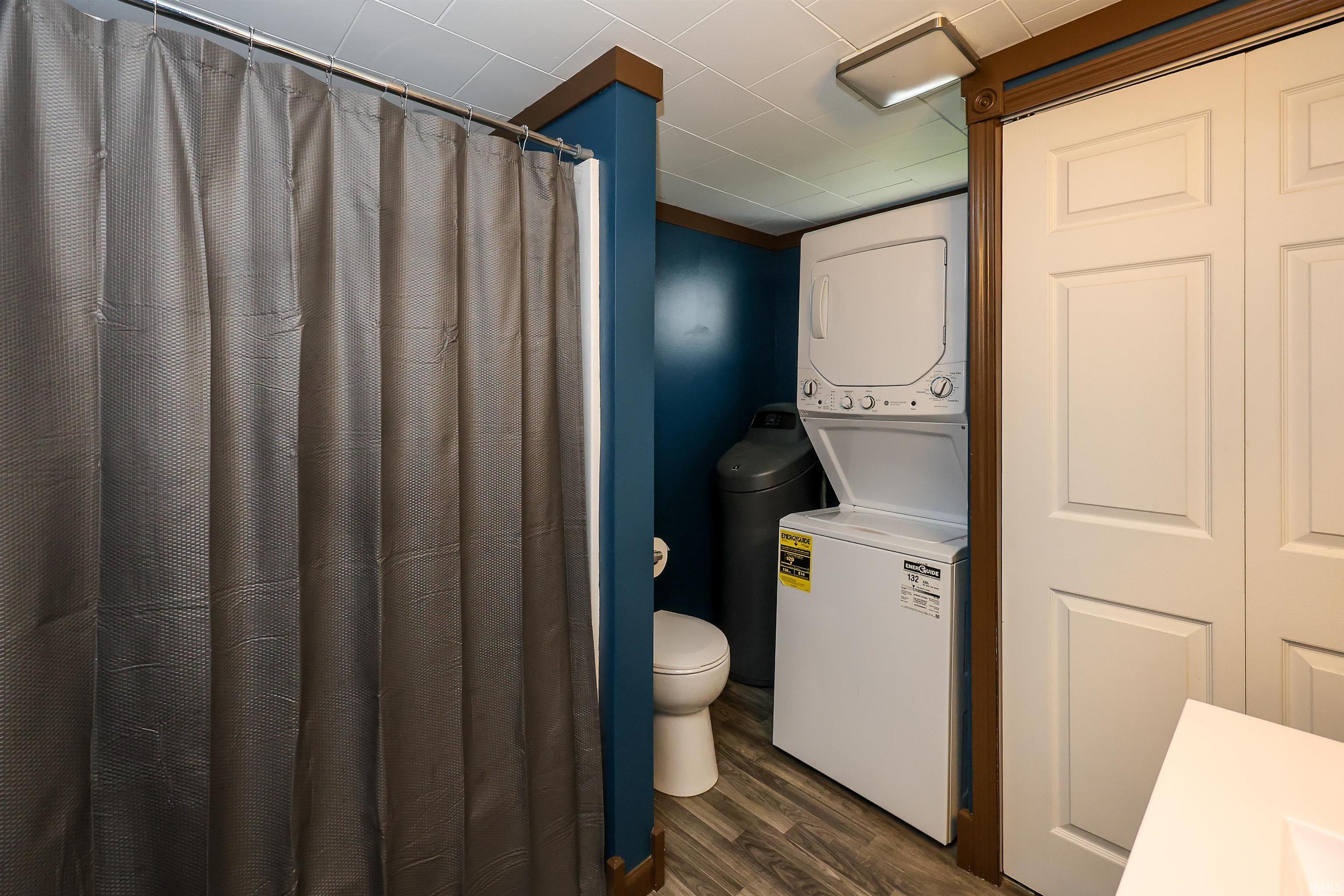 Bathroom featuring a shower with curtain, stacked washer / drying machine, dark wood-style floors, and vanity