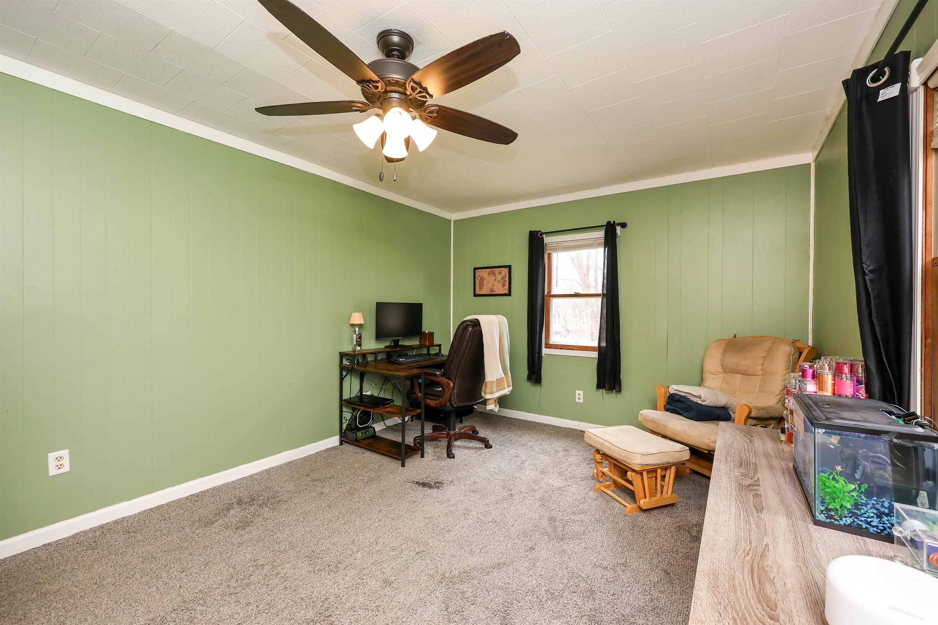 Home office with light colored carpet, ceiling fan, ornamental molding, and wooden walls