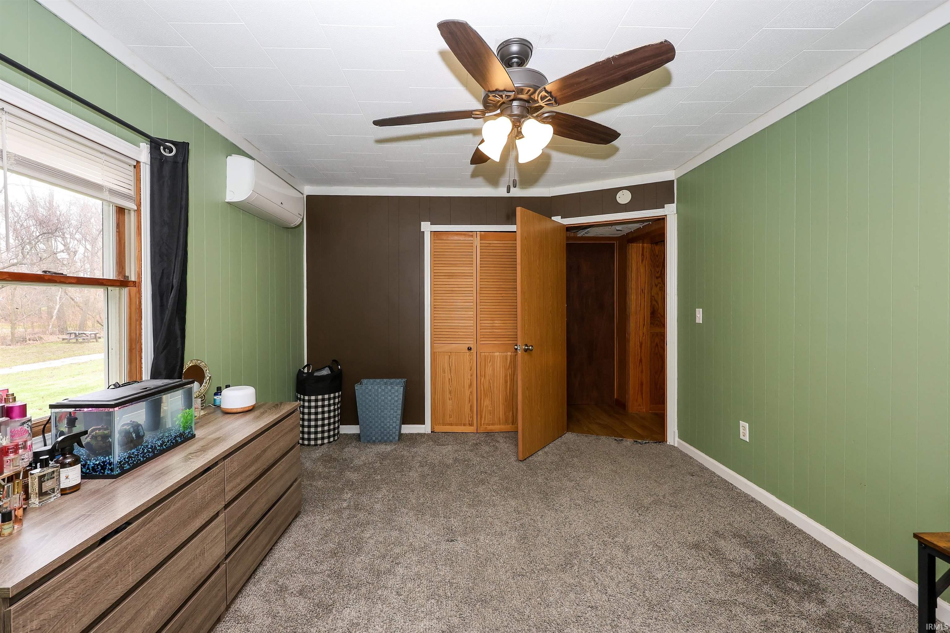 Bedroom featuring light colored carpet, wood walls, a ceiling fan, ornamental molding, and a closet