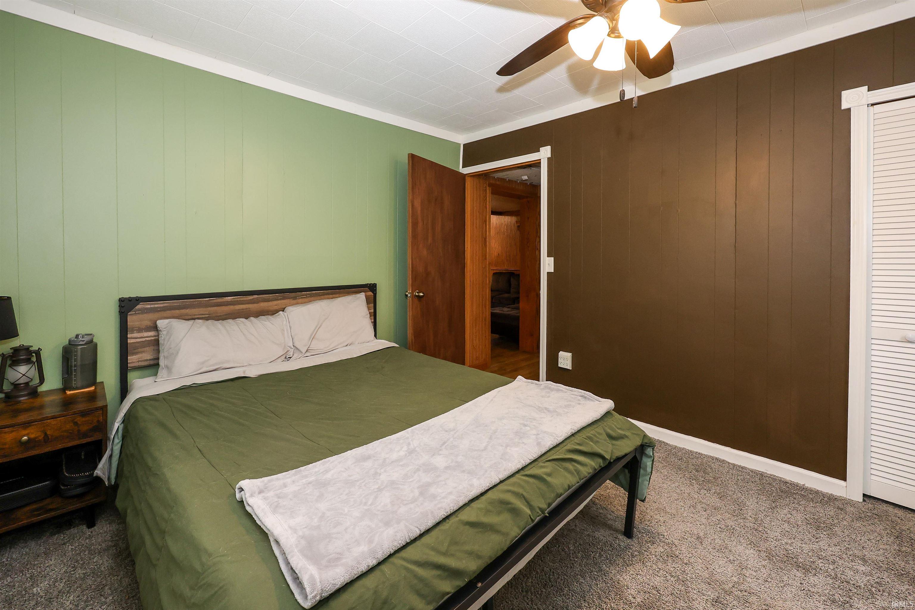 Bedroom with carpet floors, wood walls, ceiling fan, and crown molding