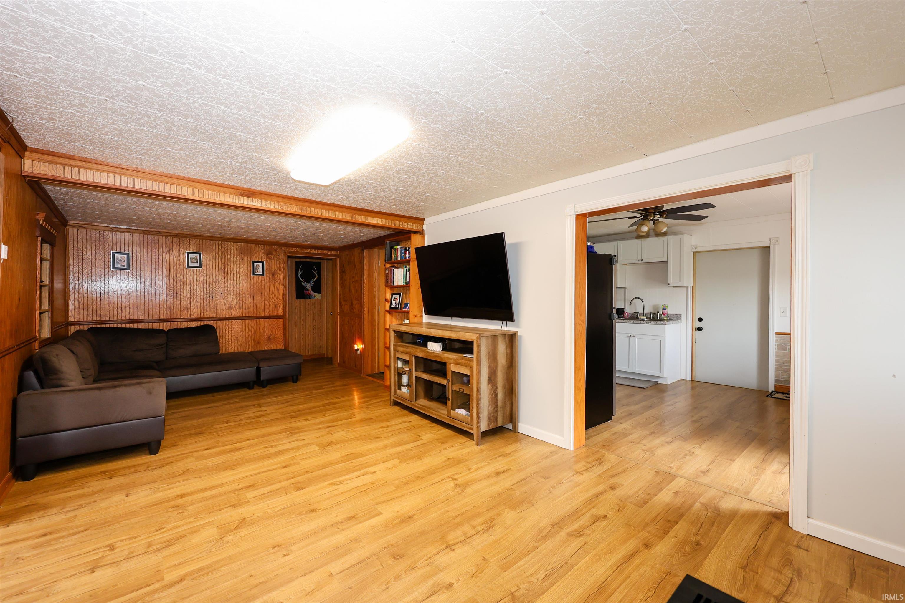 Living room featuring wooden walls, light wood-type flooring, a ceiling fan, and ornamental molding