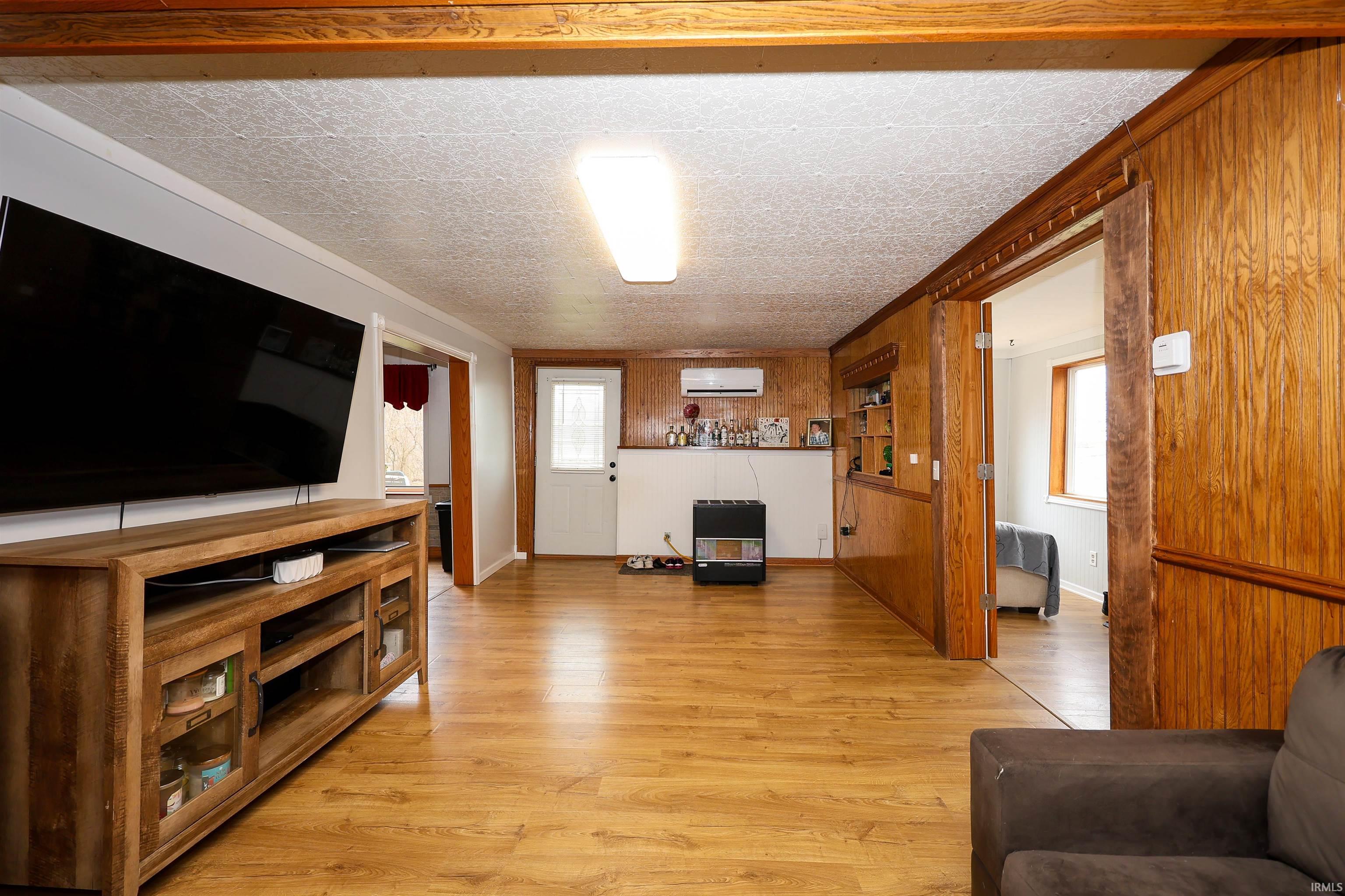 Living area featuring light wood-style floors, healthy amount of natural light, wooden walls, and ornamental molding