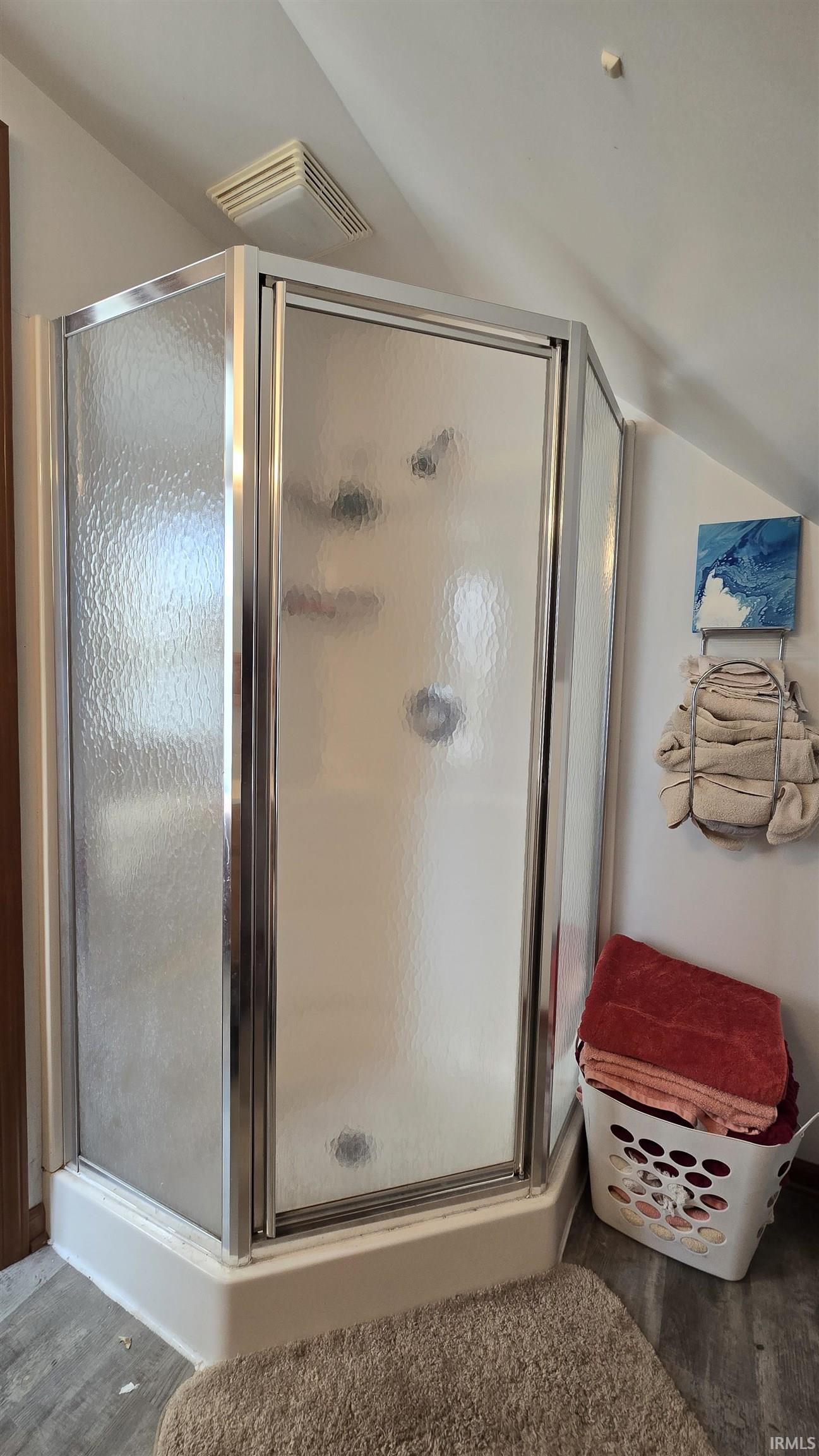 Bathroom with lofted ceiling, a shower stall, and wood finished floors