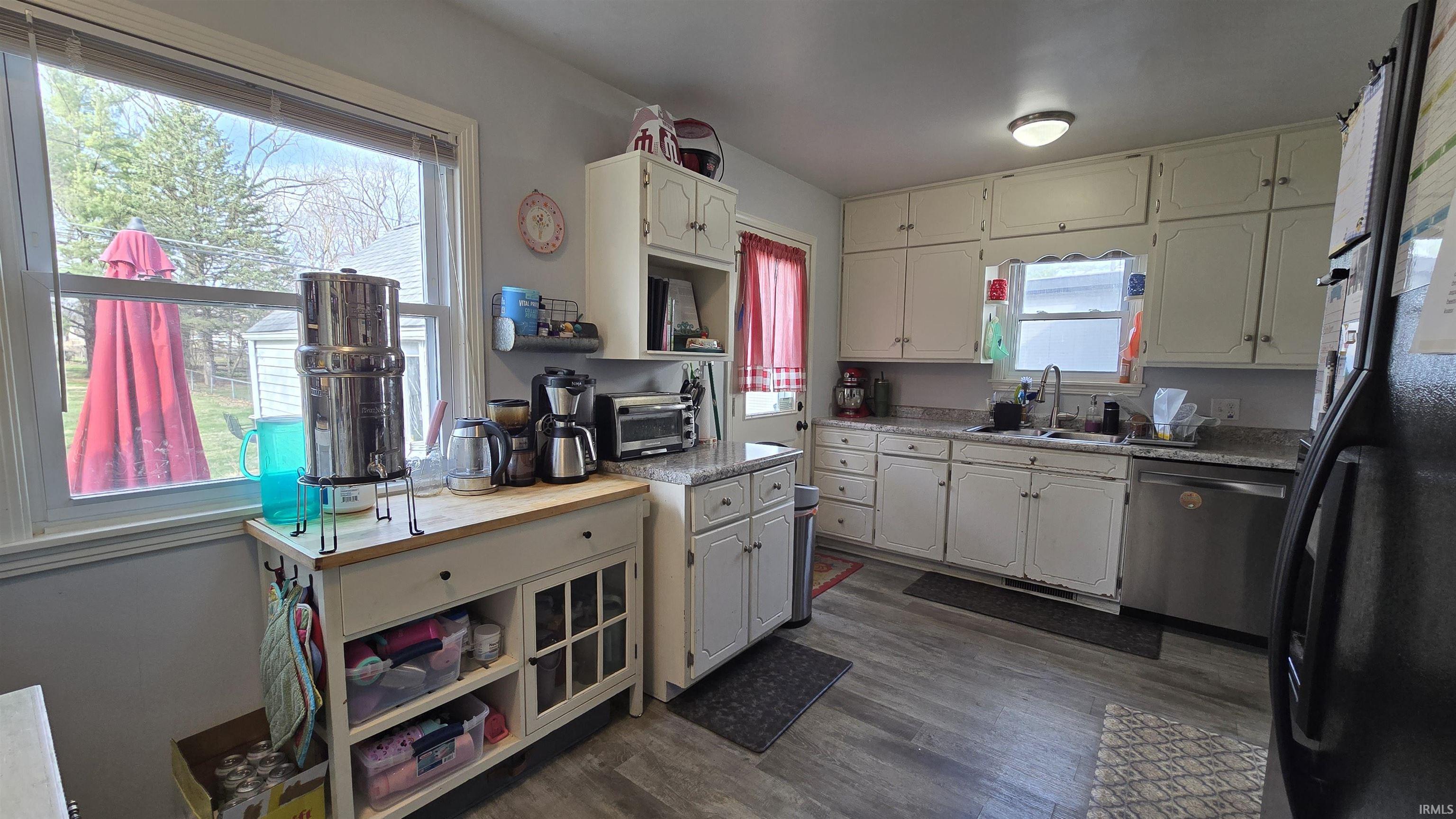 Kitchen with freestanding refrigerator, light countertops, stainless steel dishwasher, white cabinetry, and dark wood-style floors