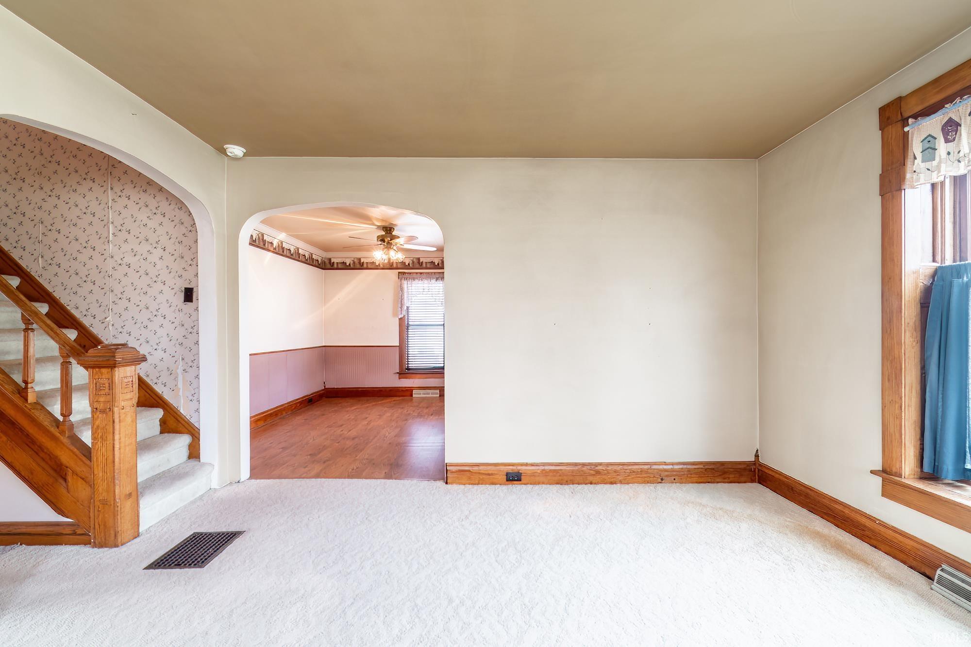 Carpeted empty room with arched walkways, a ceiling fan, and wainscoting