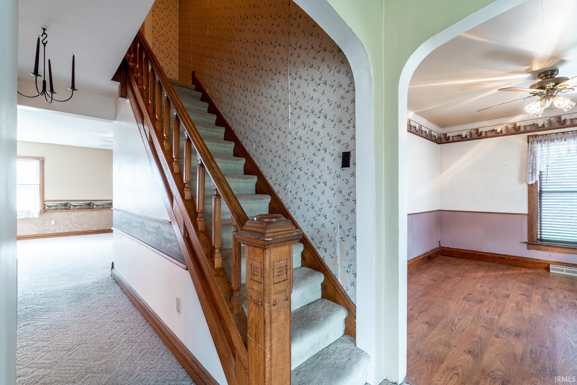 Stairs featuring hand carved wood, plenty of natural light, wallpapered walls, arched walkways, ceiling fan, and a wainscoted wall