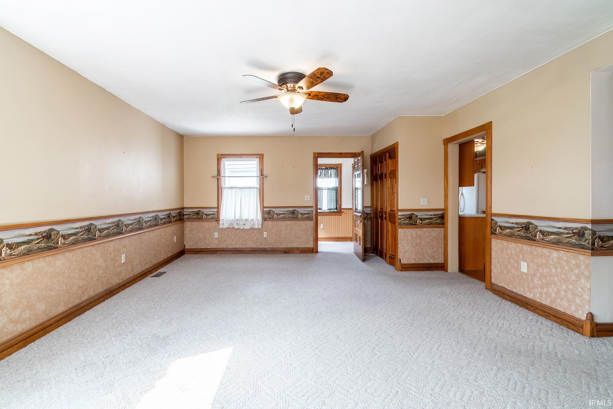 Spacious great room featuring wainscoting, ceiling fan, light colored carpet, and wallpapered walls