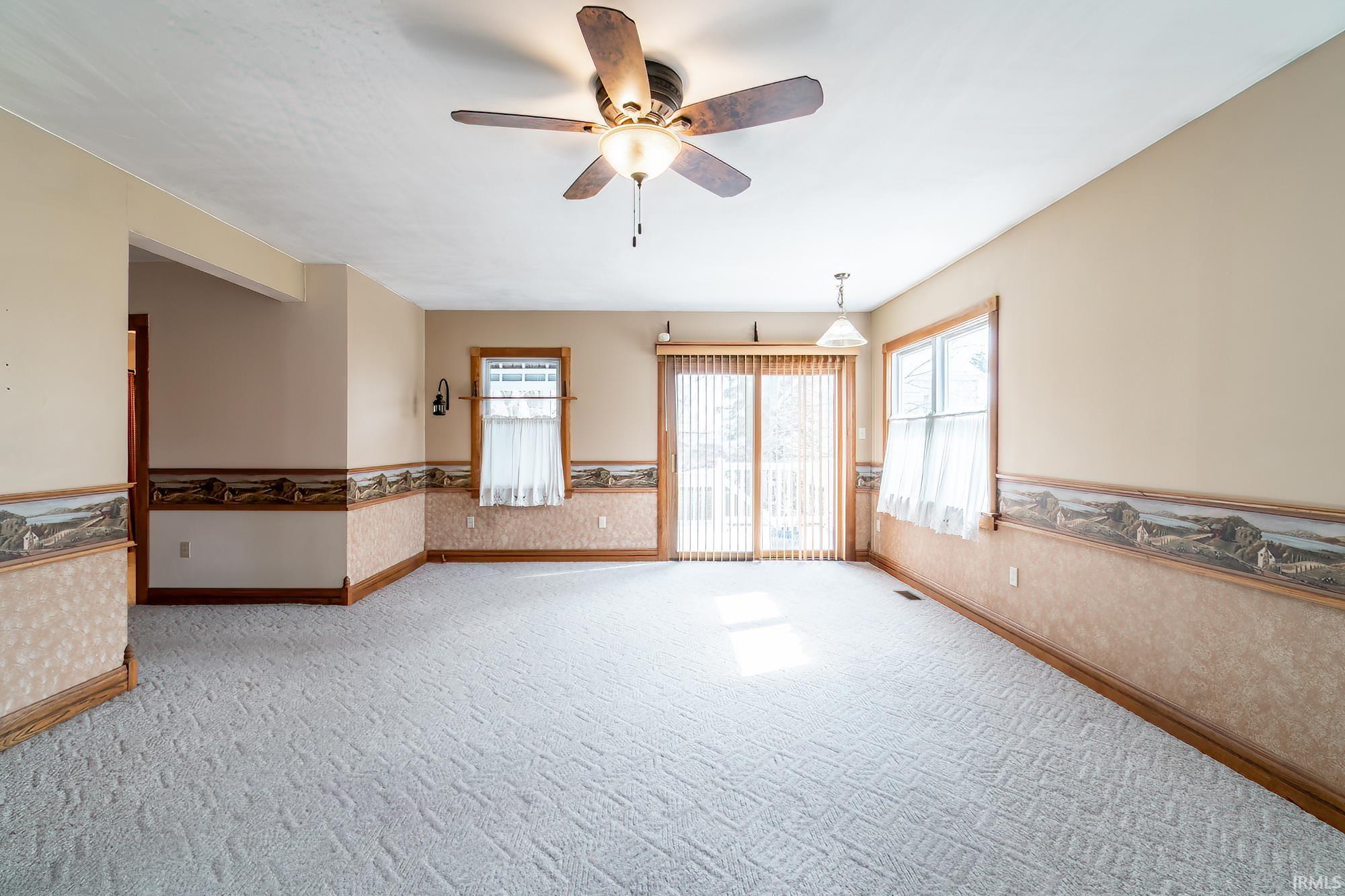 Great room with access to outdoor patio and sunroom.  This room features a wainscoted wall, a ceiling fan, carpet floors, healthy amount of natural light, and wallpapered walls
