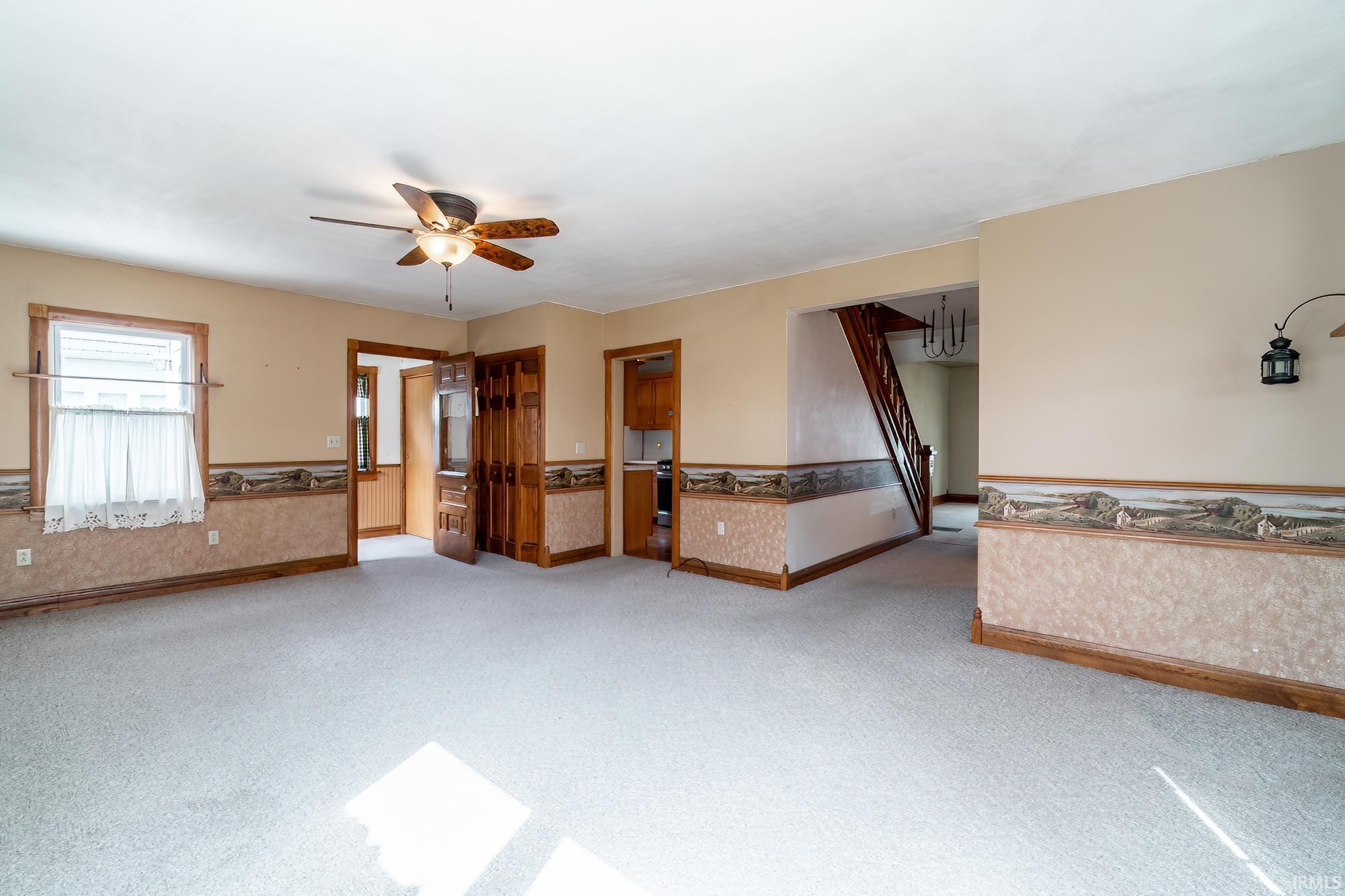 Great room featuring light carpet, a wainscoted wall, and a ceiling fan