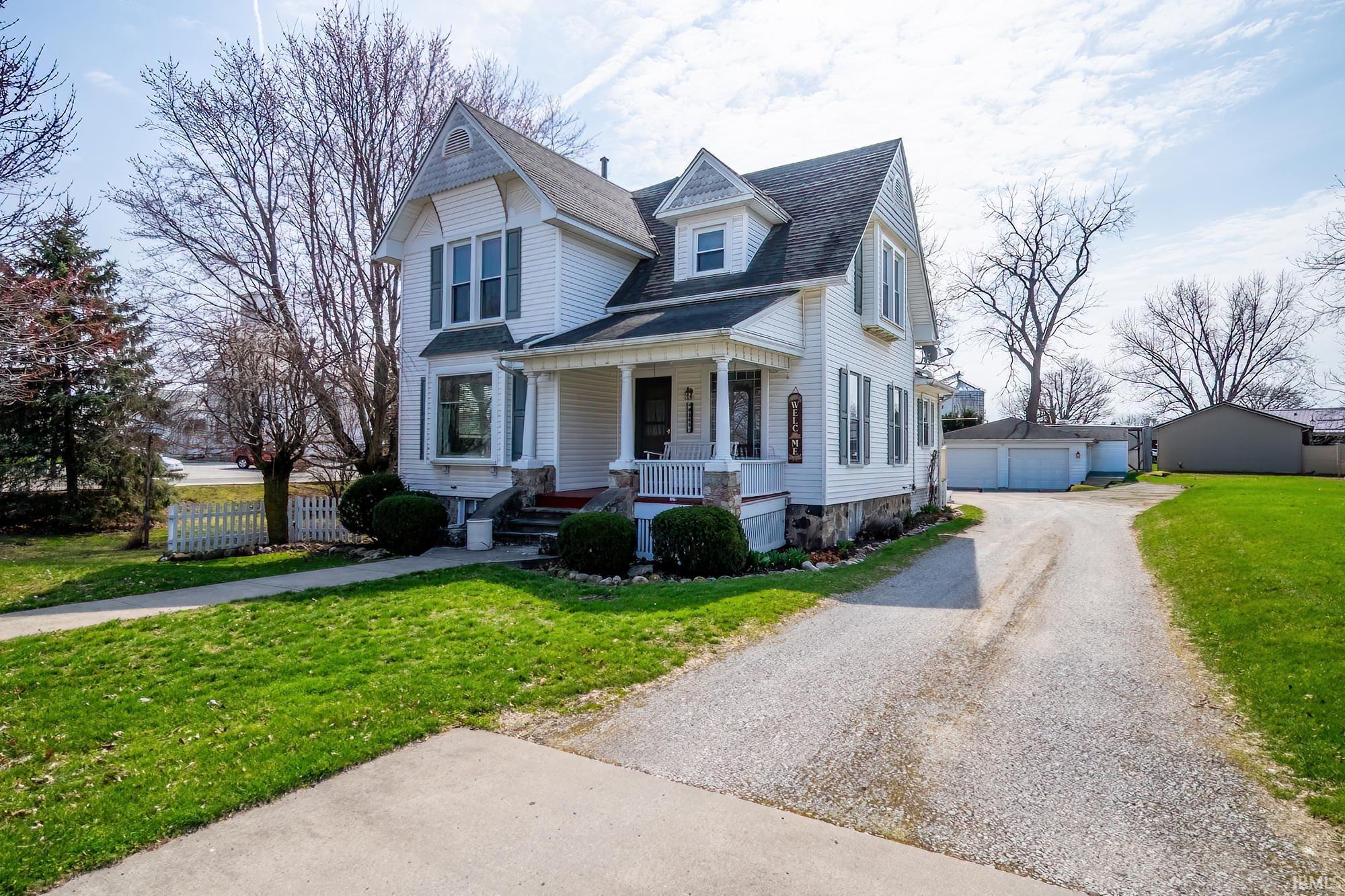 Victorian house with a front yard, sidewalk, covered porch, and detached 2-car garage.