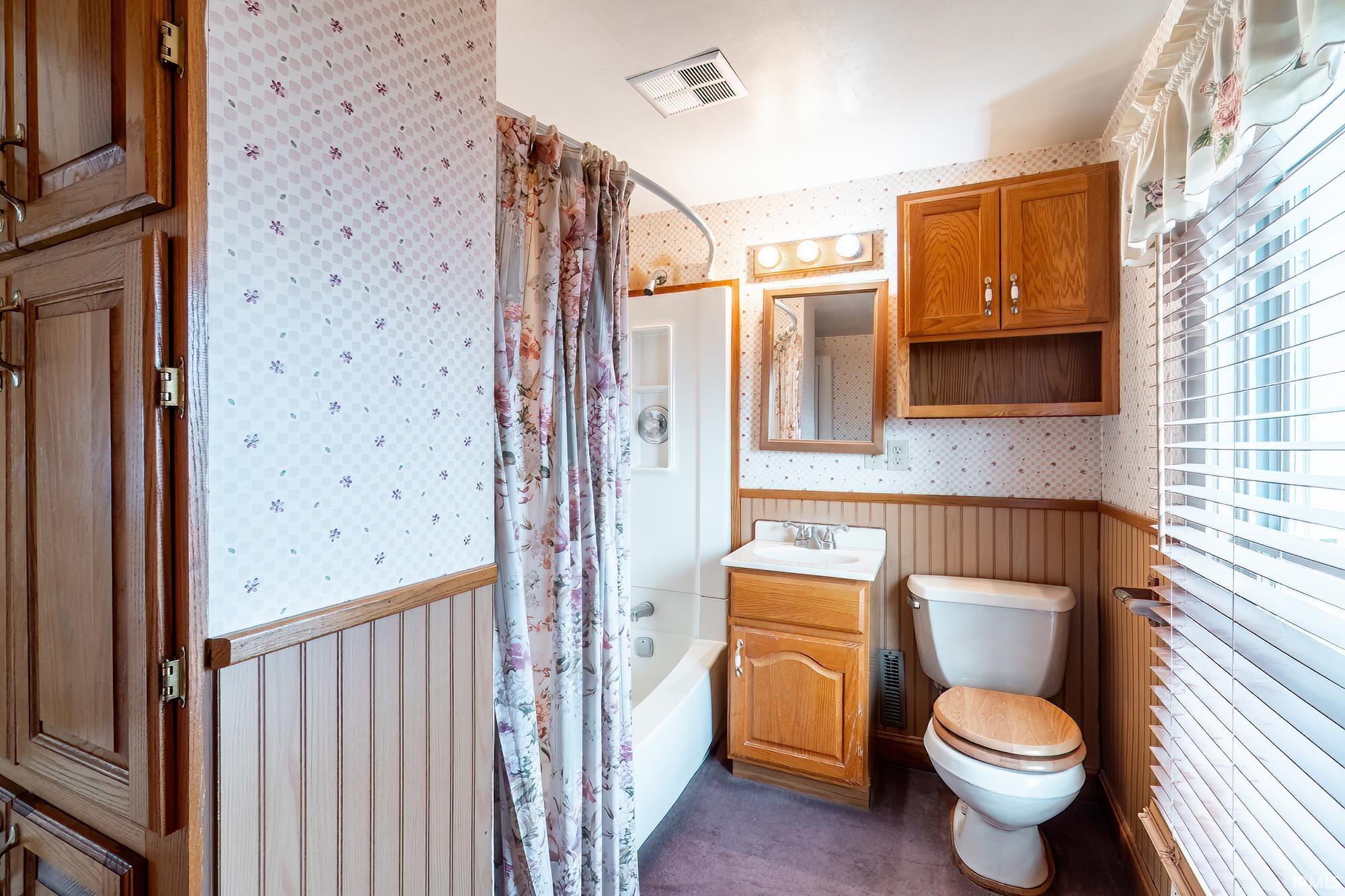 Bathroom featuring wallpapered walls, a wainscoted wall, vanity, and shower / tub combo with curtain