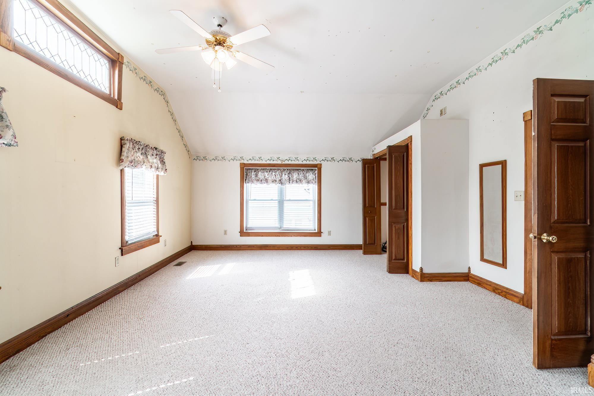 Primary Bedroom with light colored carpet, a ceiling fan, and lofted ceiling